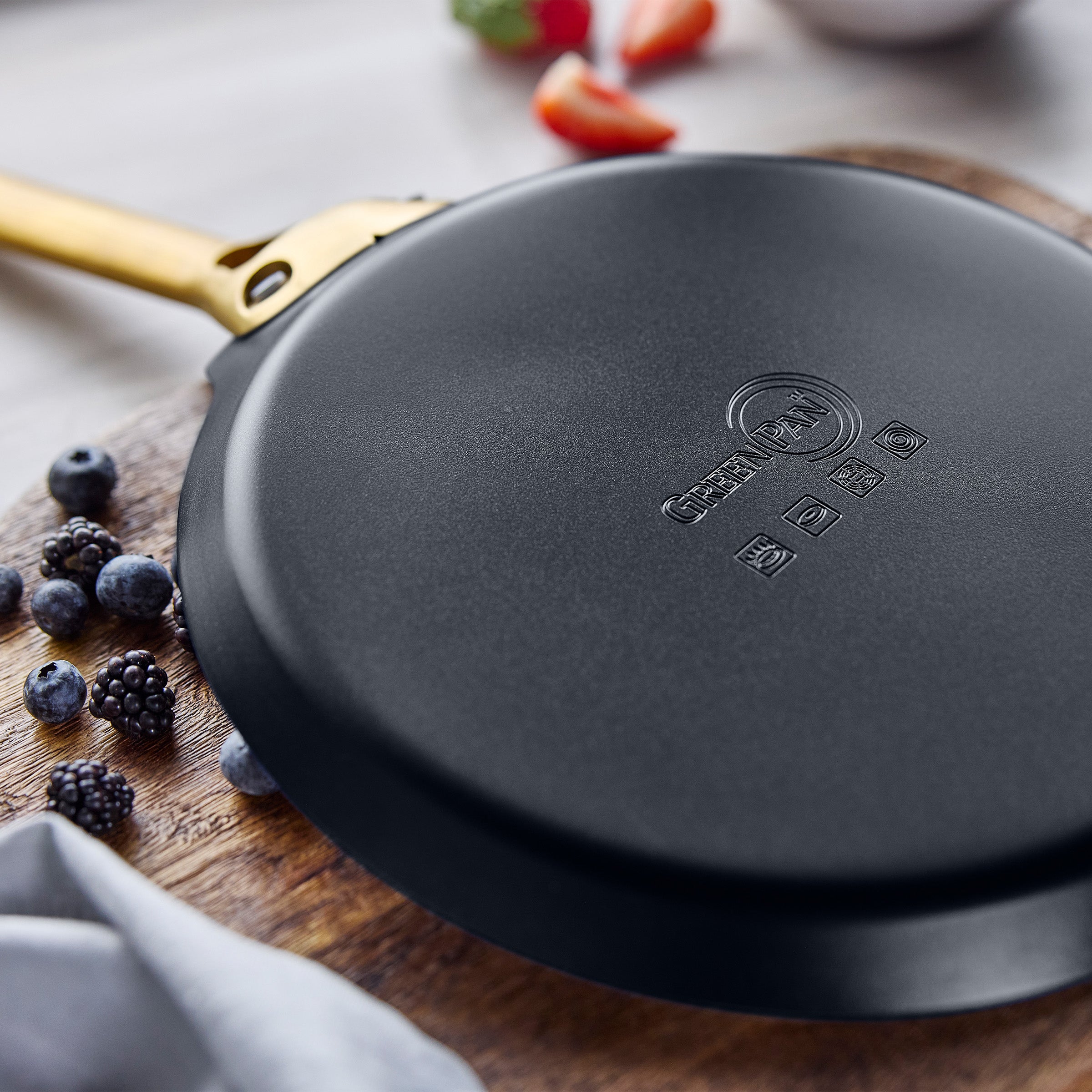Black crepe pan on a wooden surface with berries and a cloth