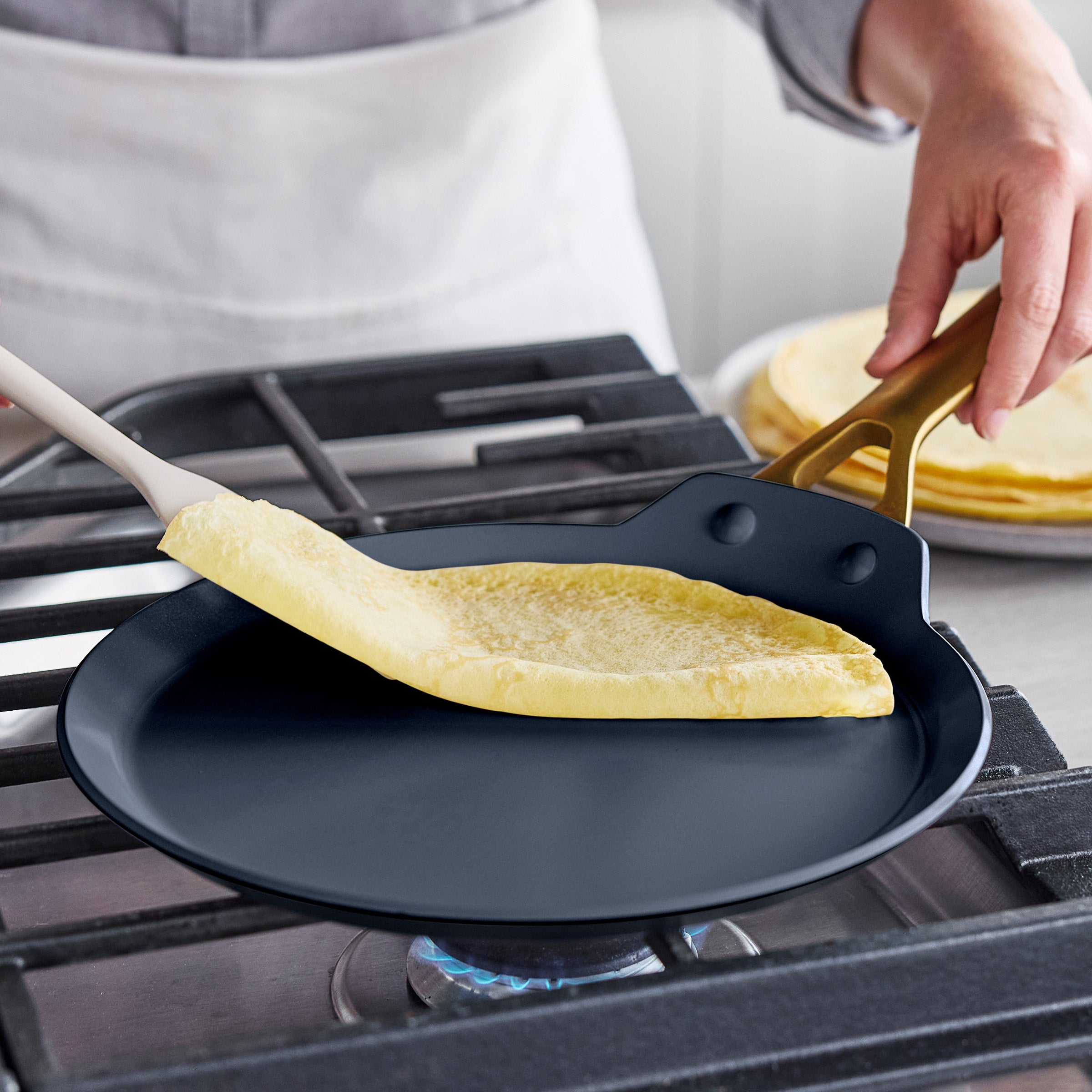 Person cooking a crepe on a stove with a spatula