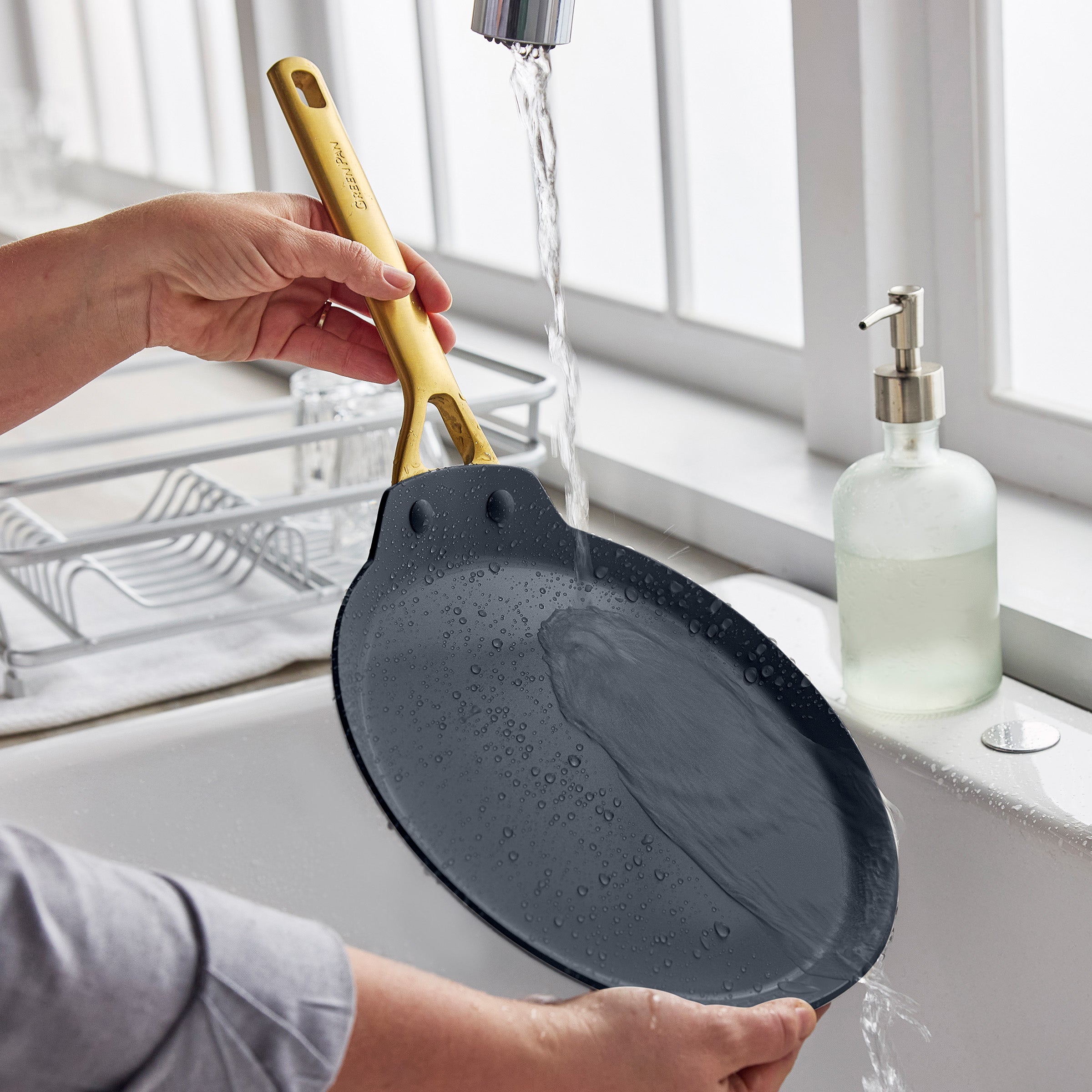 Person washing a black crepe pan under running water in a kitchen sink