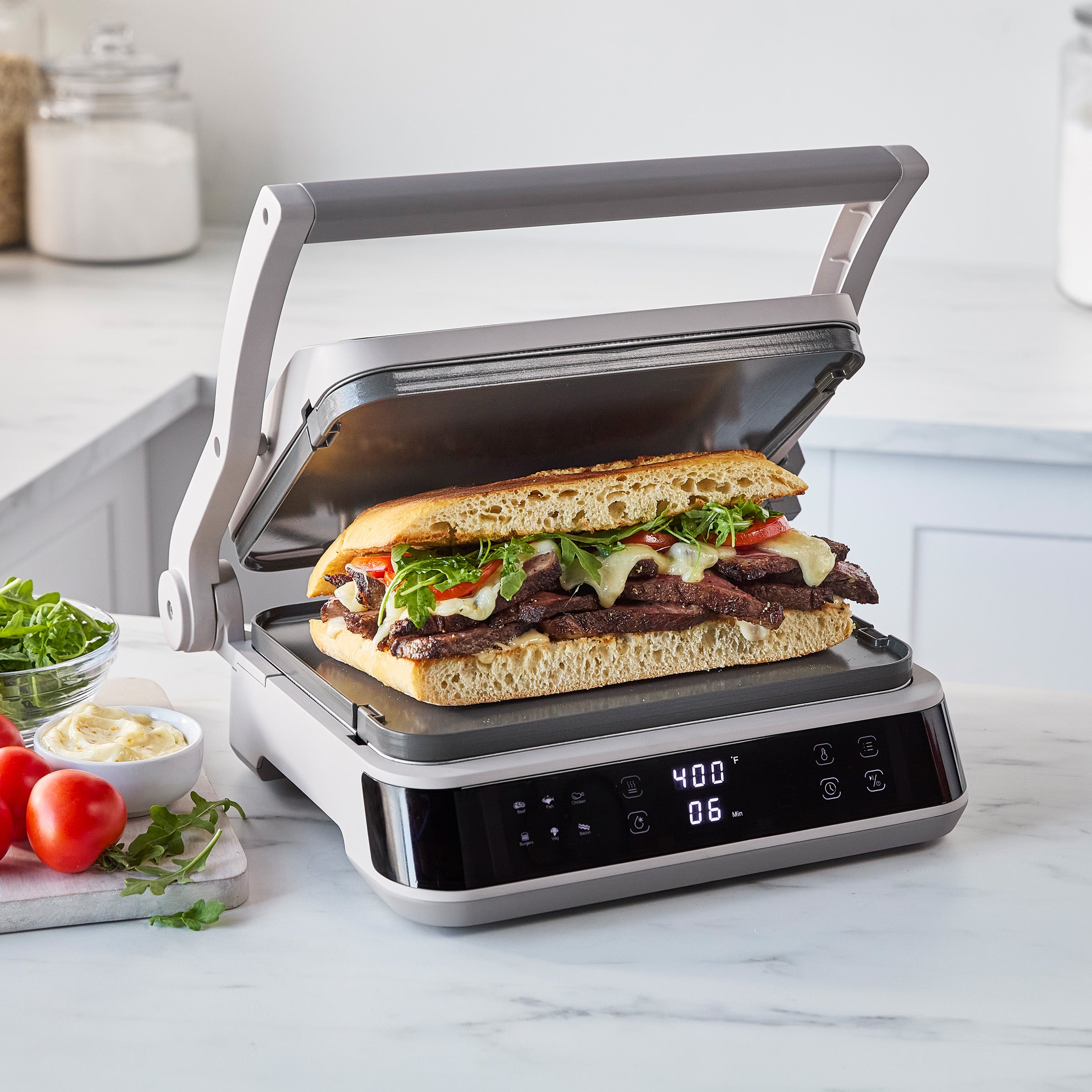 Clay grill and griddle cooking a sandwich with meat, cheese, and greens on a kitchen counter at 400°F.