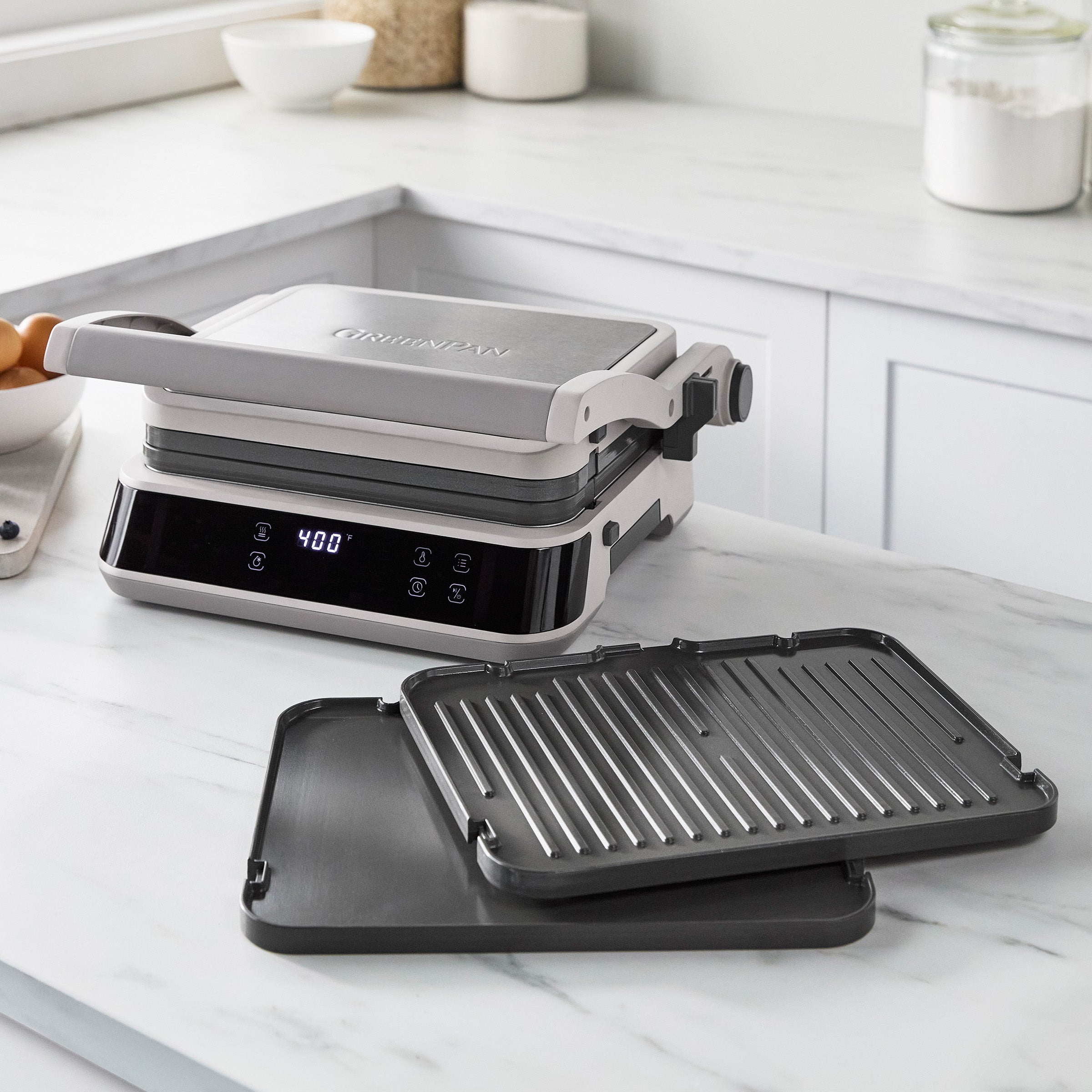 Grill and griddle with digital display, open lid, and two ceramic plates on a white kitchen counter.