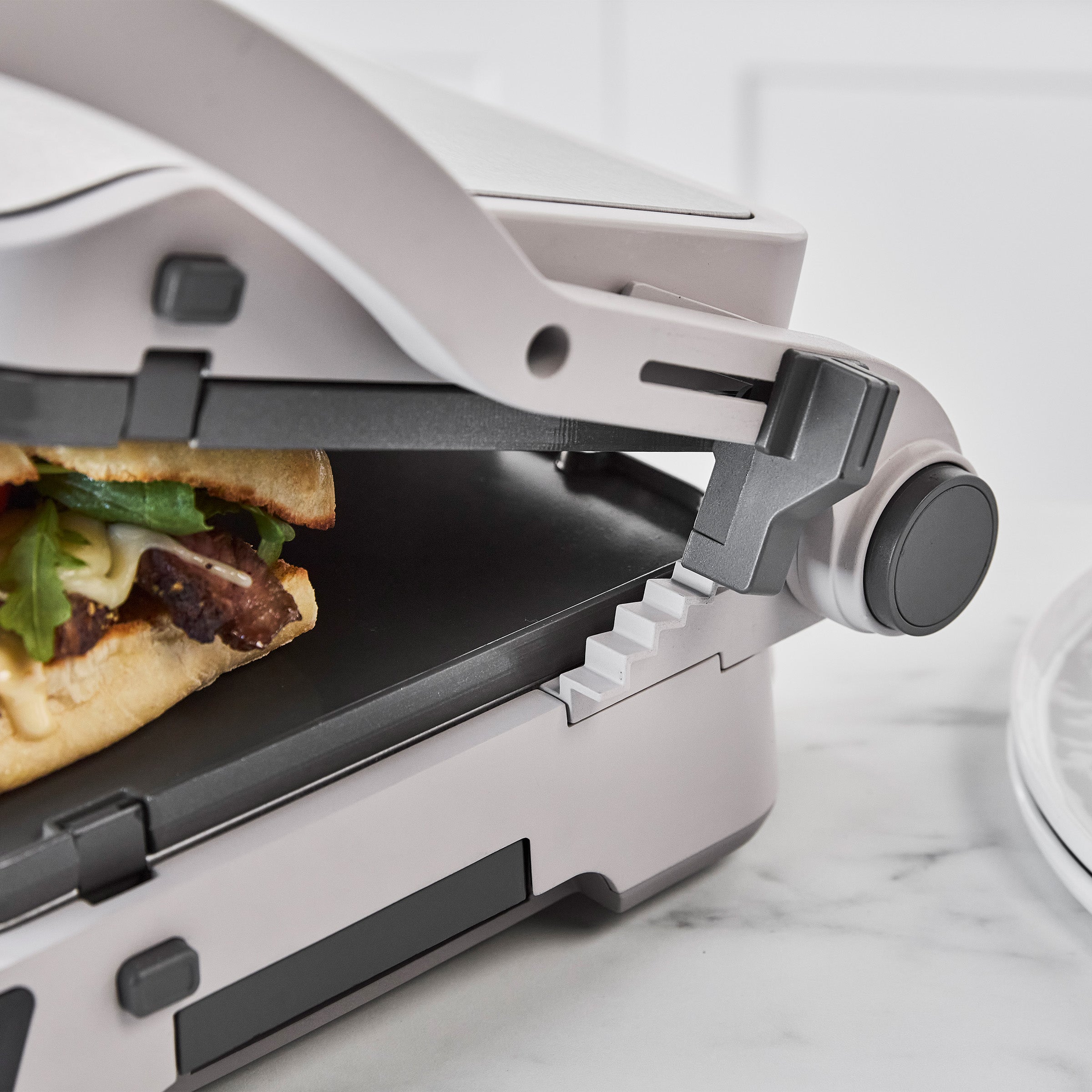 Sandwich toasting in a clay-colored grill and griddle with ceramic surface on a marble countertop.