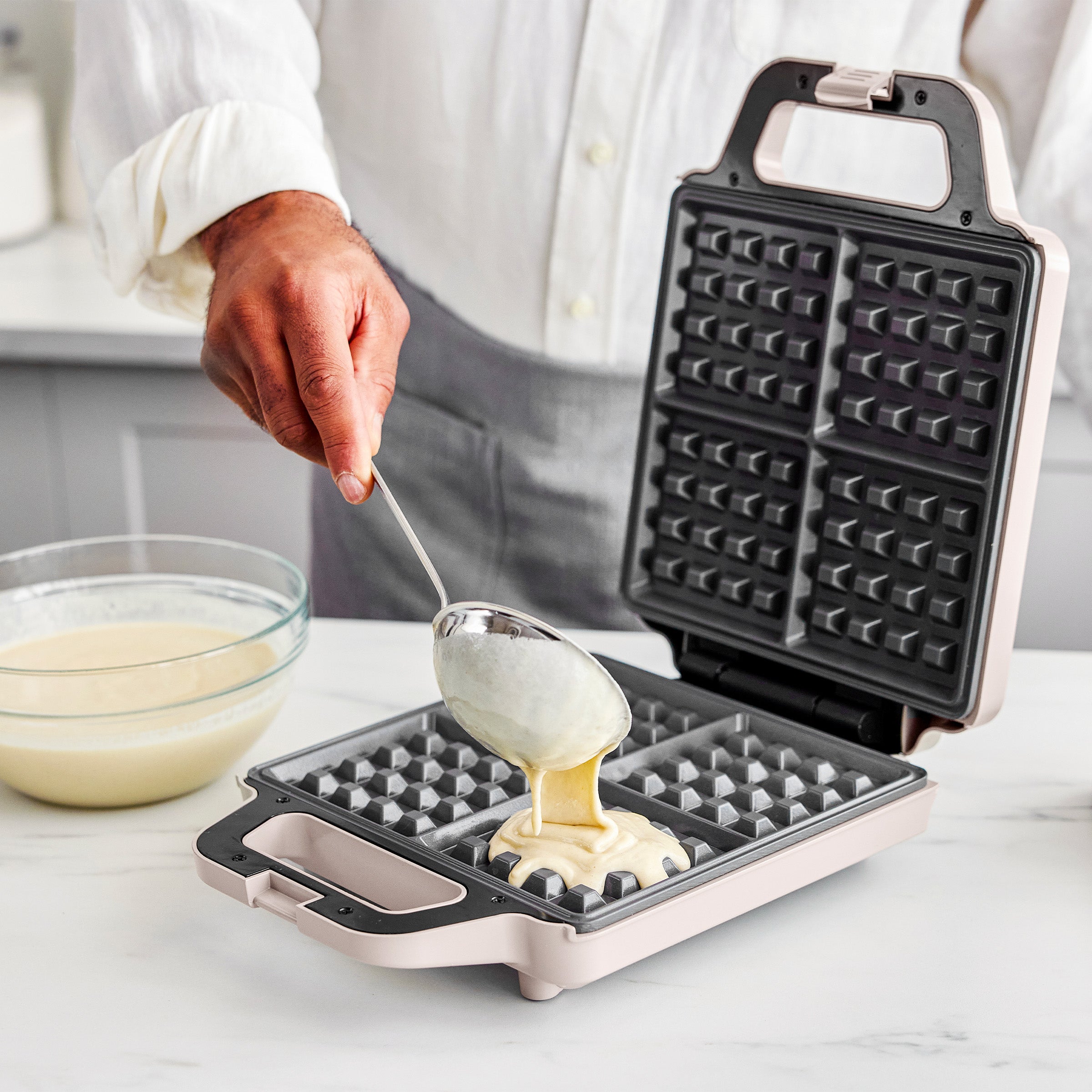 Person using a waffle maker with batter being poured into it