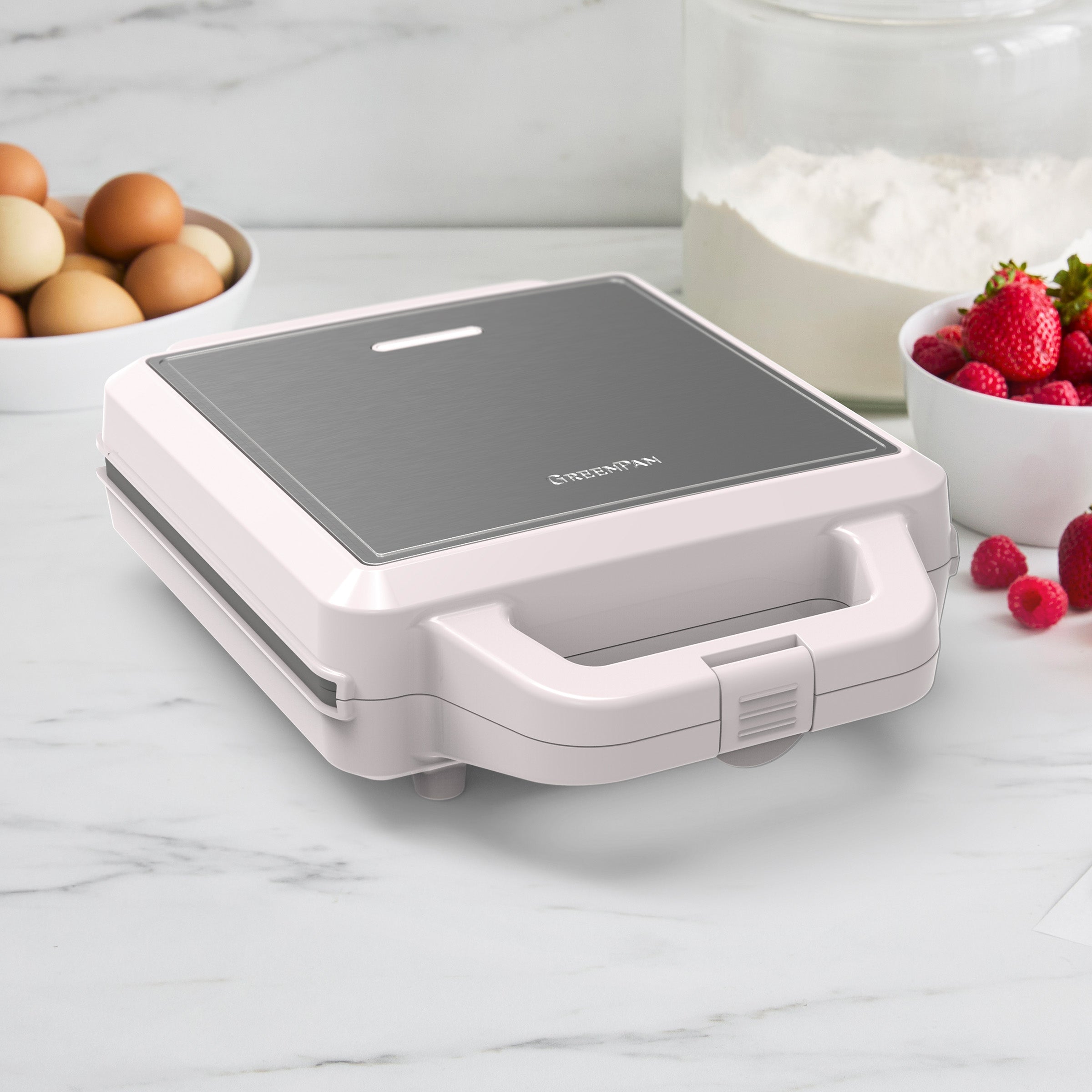Taupe waffle maker on a marble countertop with ingredients in the background