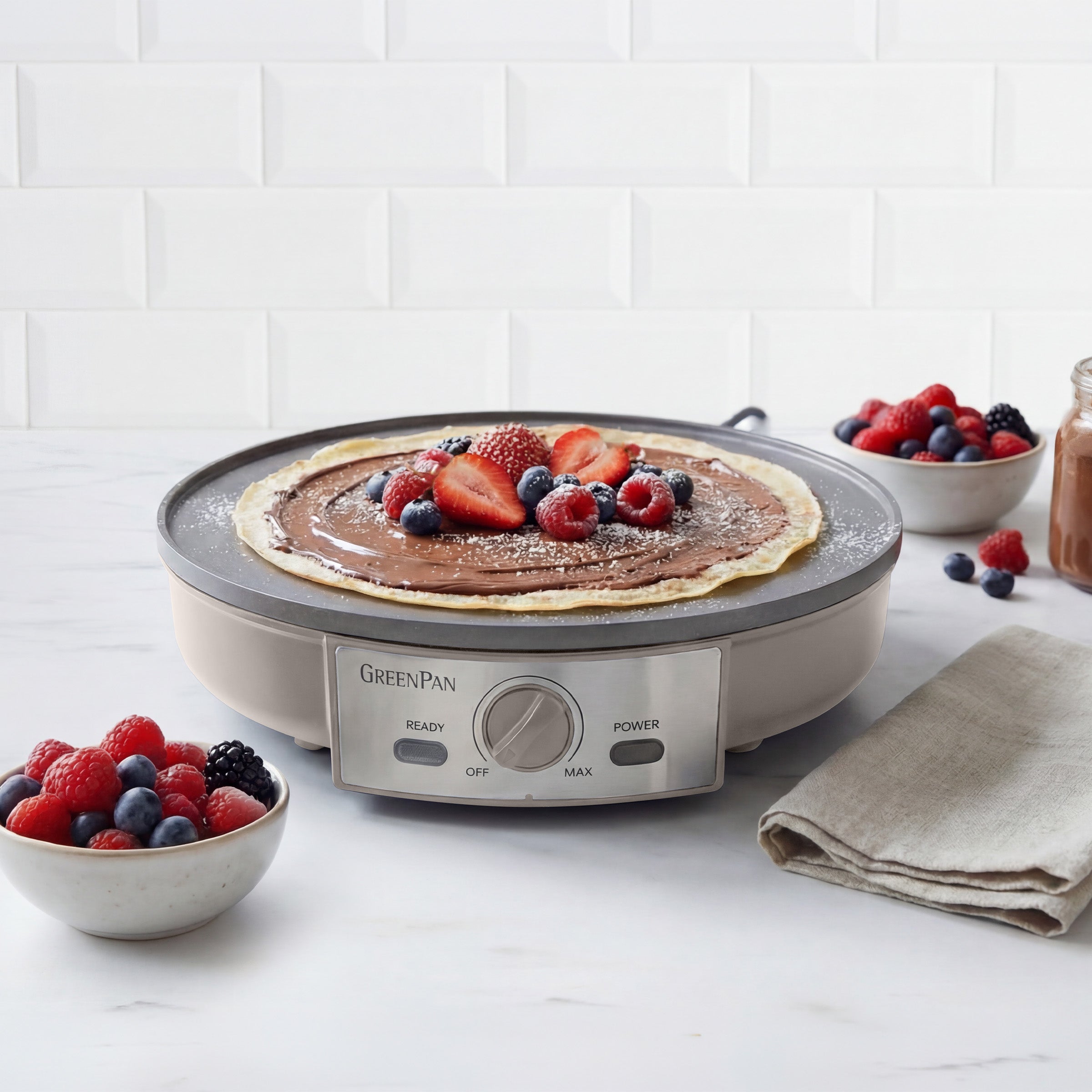 Electric crepe maker with a cooked pancake and berries on a white surface.