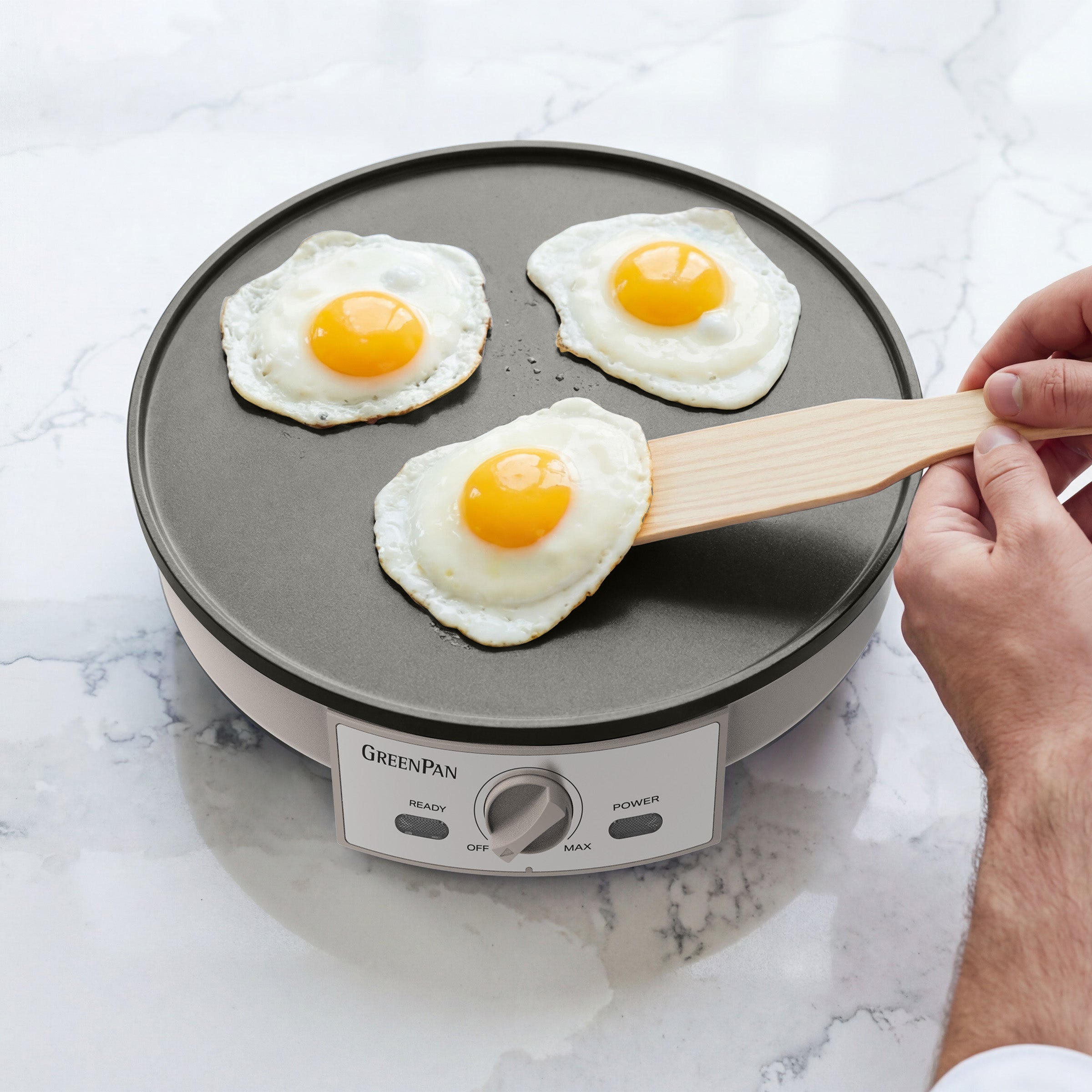 Person flipping eggs on a GreenPan electric crepe maker on a marble countertop.