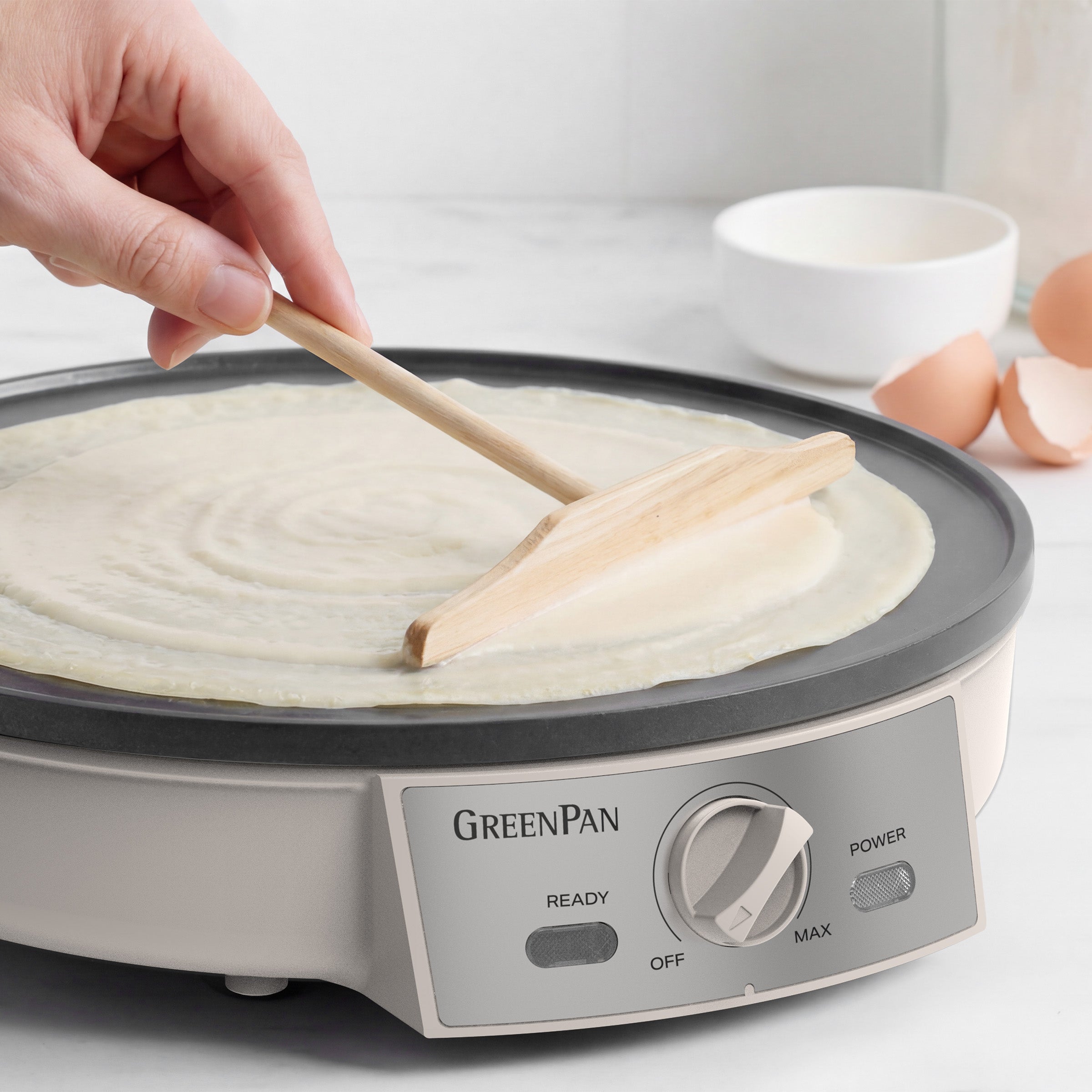 Person using a wooden spatula to spread batter on a GreenPan electric crepe maker.