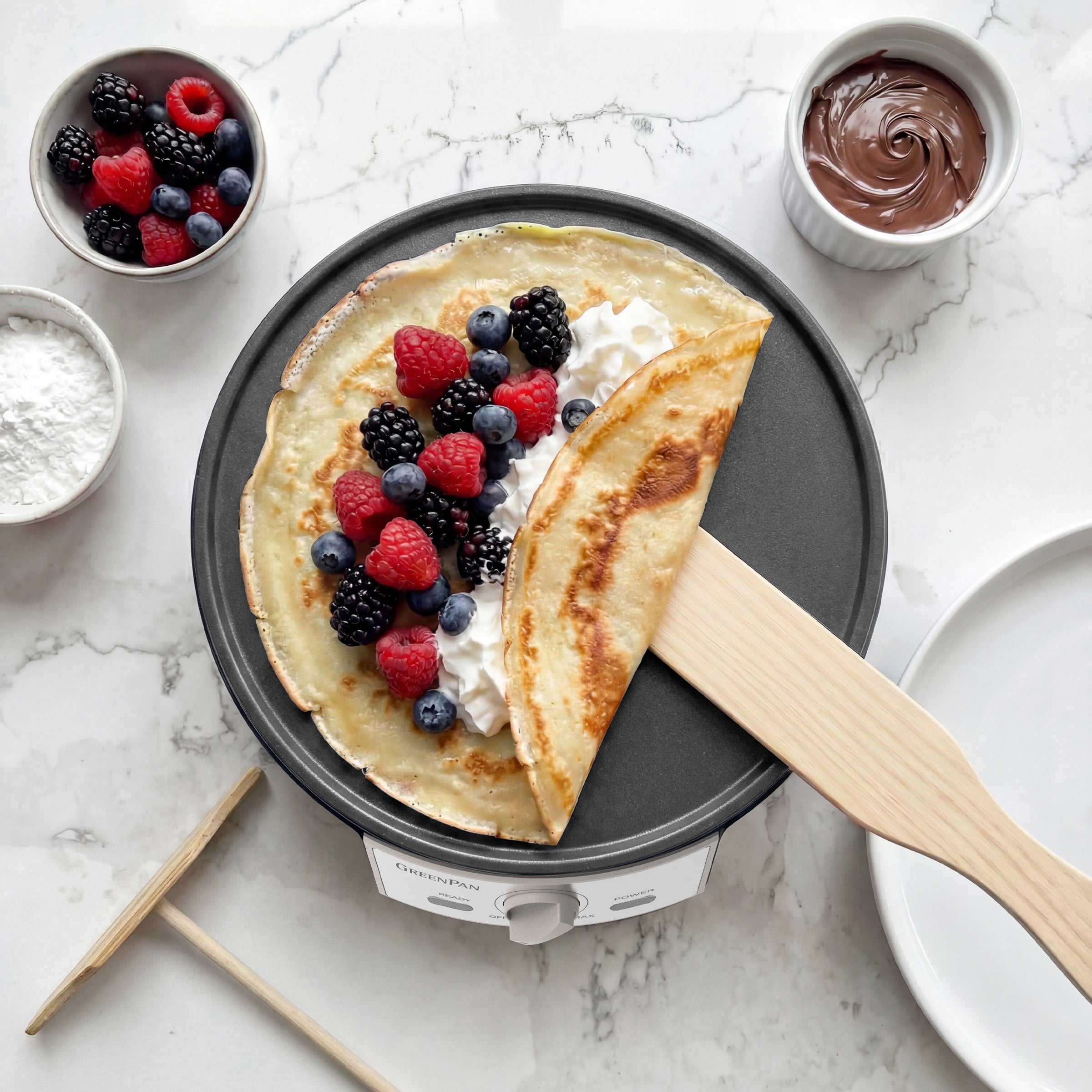 Crepe with berries on a crepe maker with ingredients around