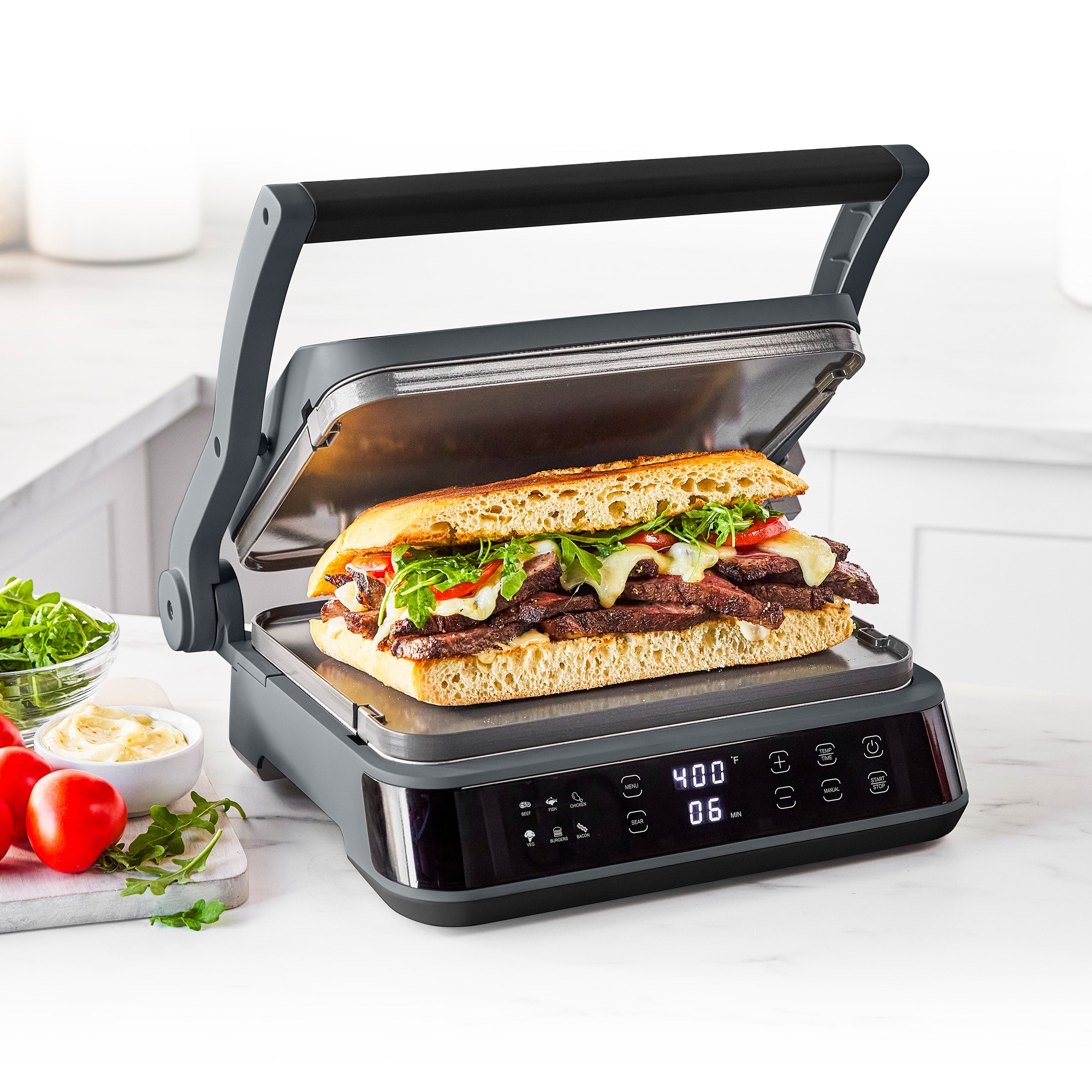 Graphite grill and griddle cooking a large sandwich with meat, cheese, and greens; digital timer shows 6 minutes remaining.