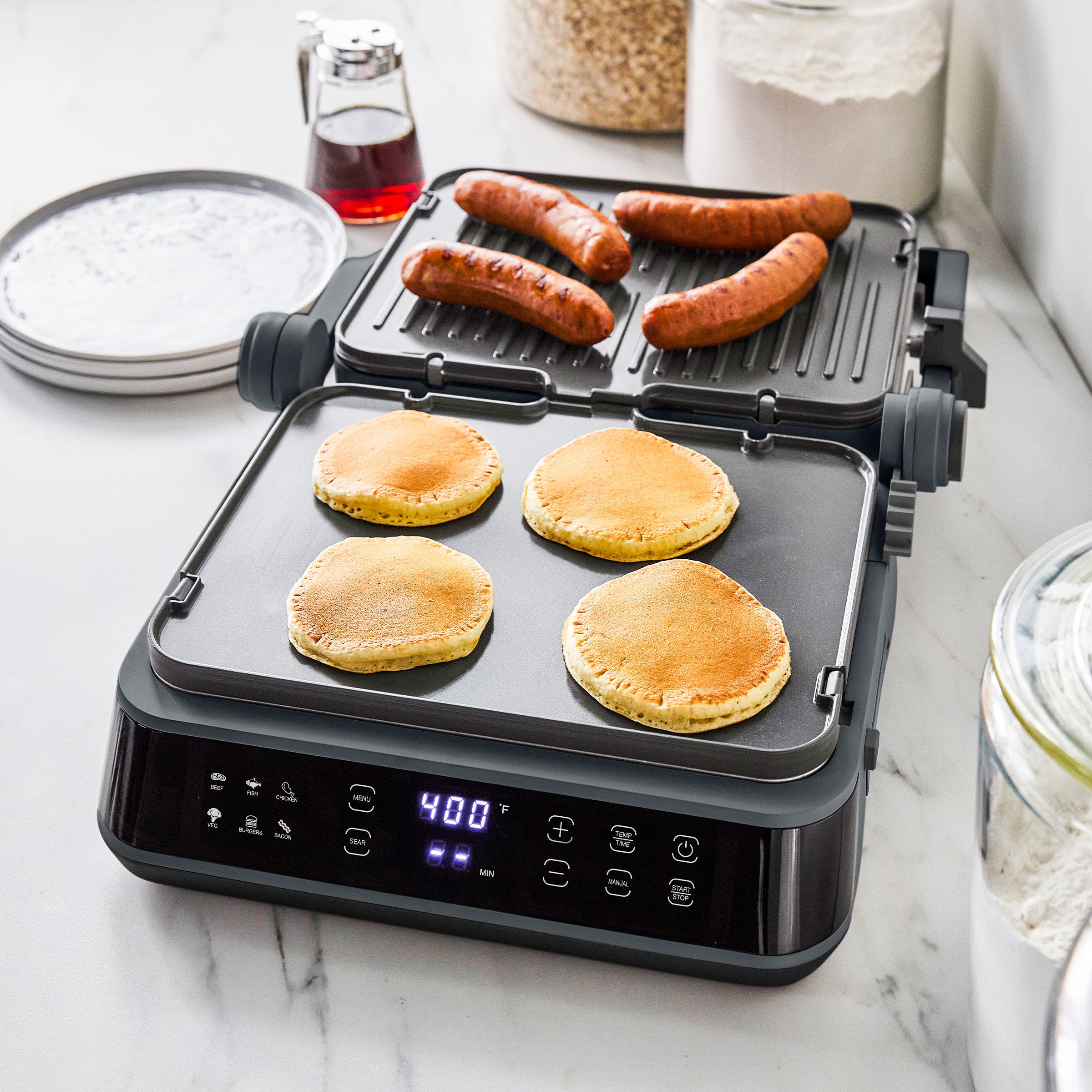 Pancakes and sausages cooking on a graphite-colored 5-in-1 grill and griddle with digital controls.