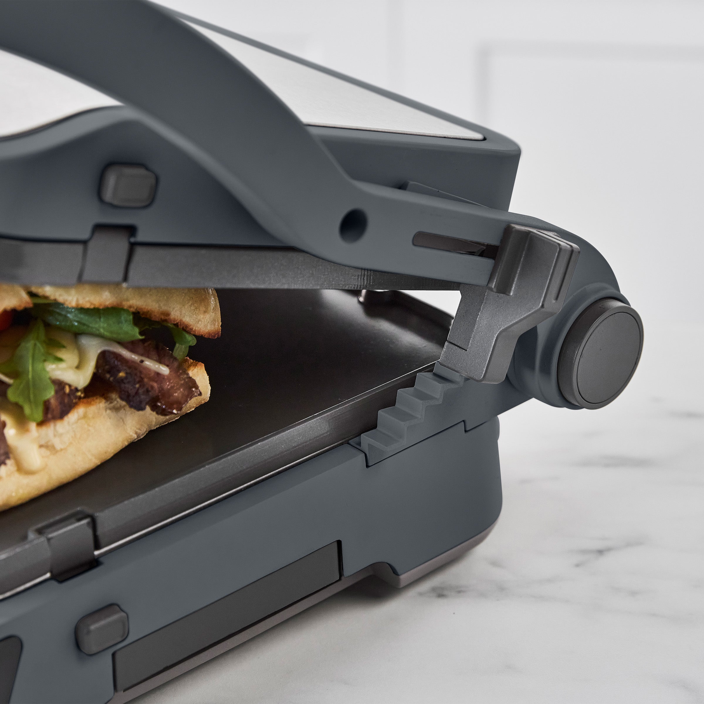 Graphite grill and griddle with ceramic nonstick plates, pressing sandwiches on a marble countertop.