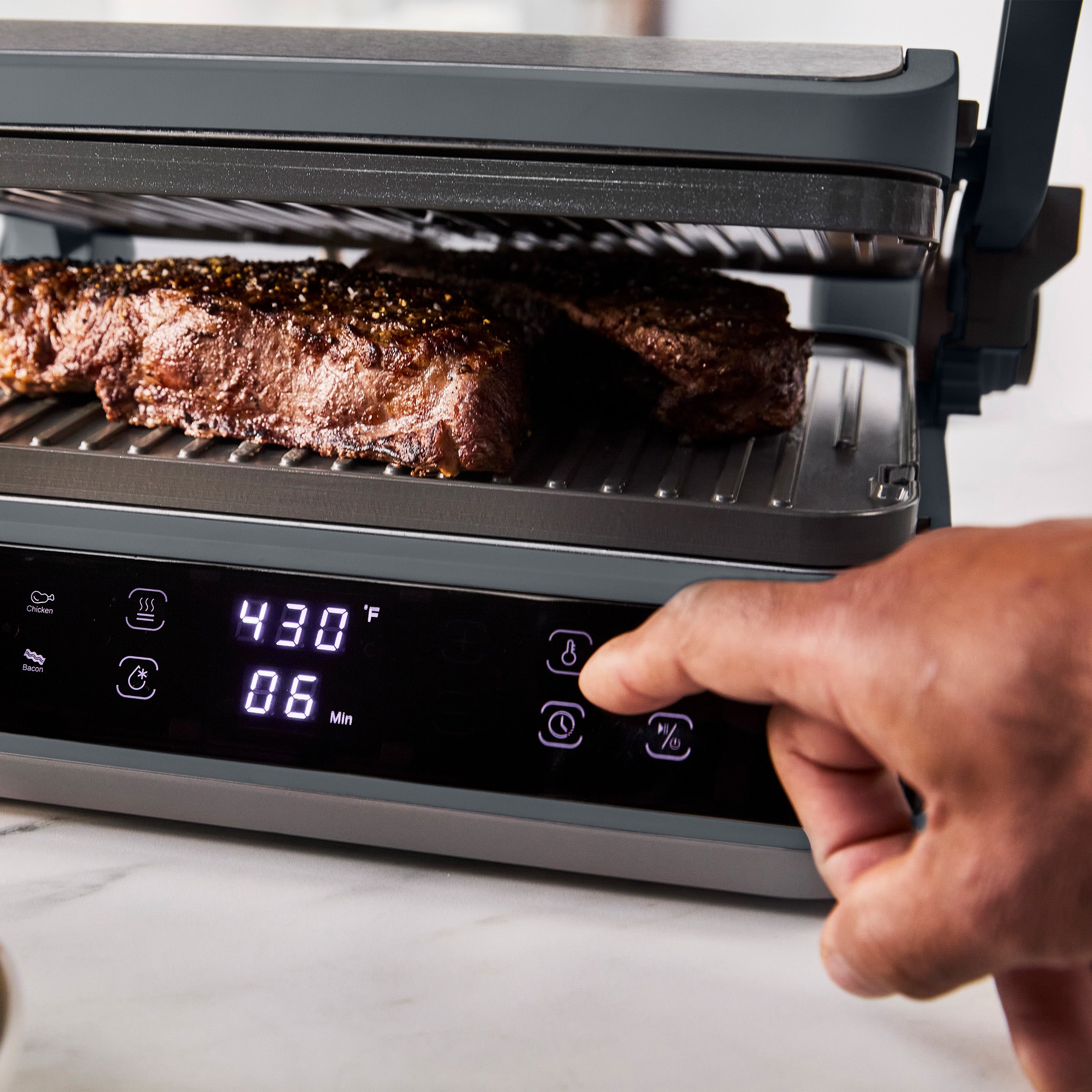 Hand grilling steaks on graphite Advanced Grill and Griddle, digital display shows 430°F and 6 minutes remaining.