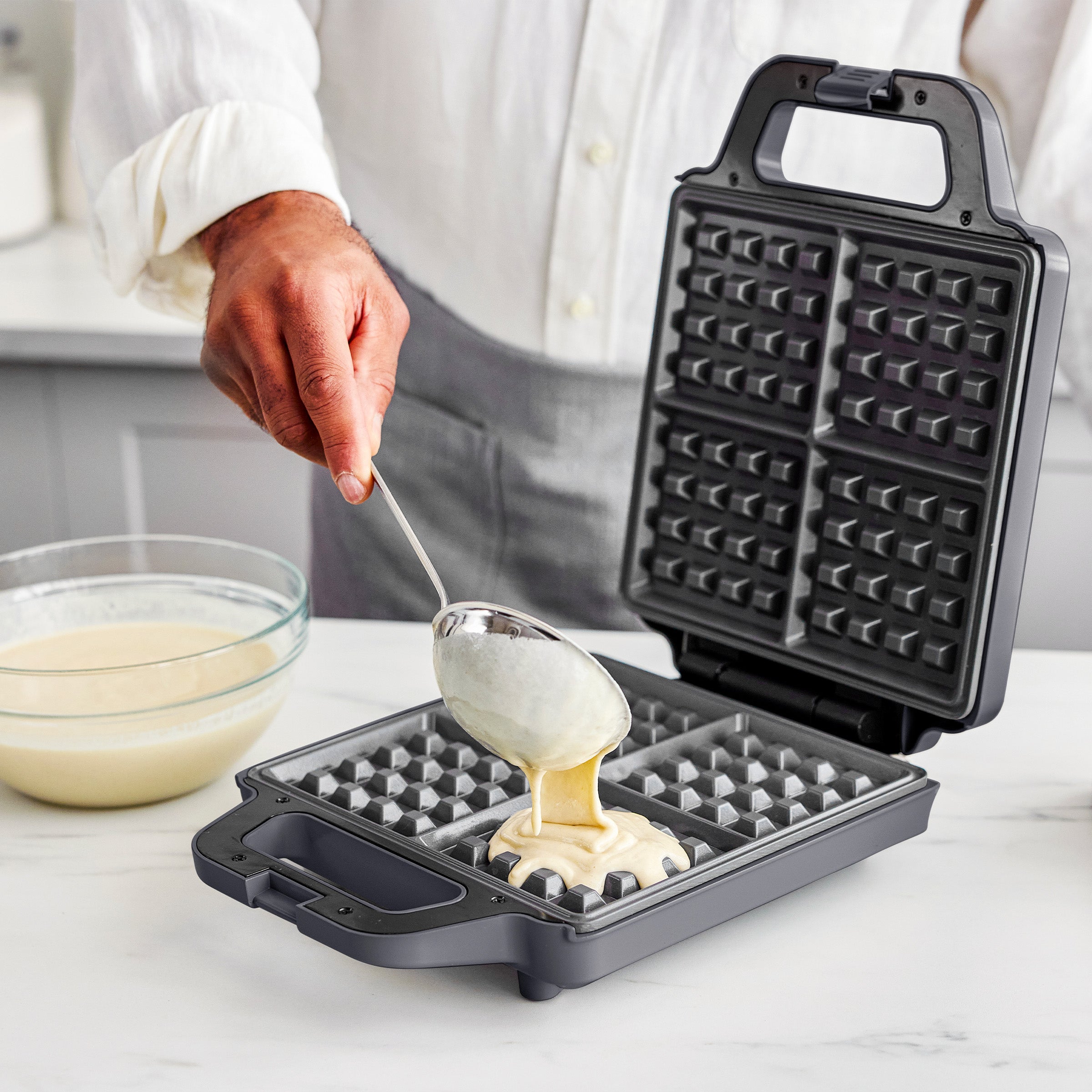 Person making waffles using a waffle maker with batter.