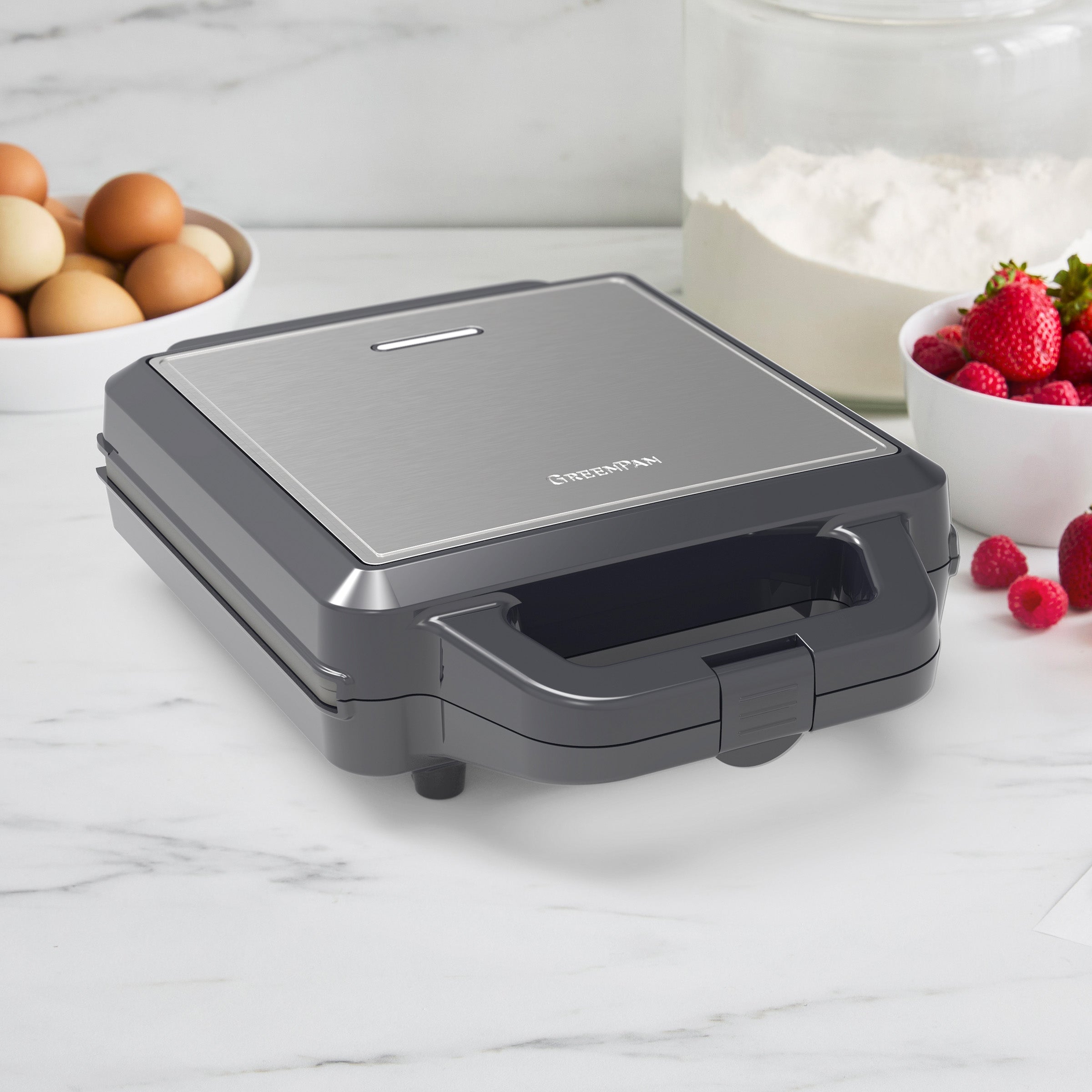 Gray waffle maker on a marble countertop with ingredients in the background