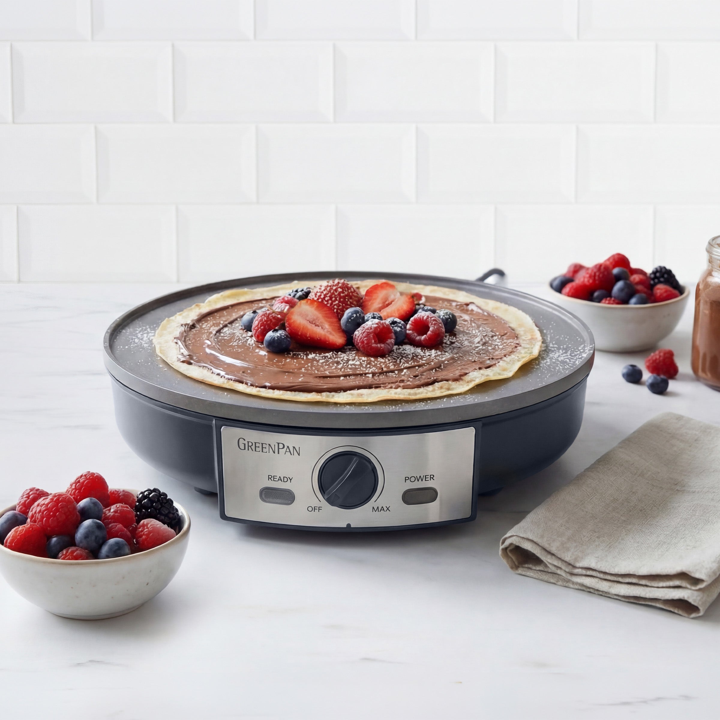 Electric crepe maker with a cooked pancake and berries on a white surface