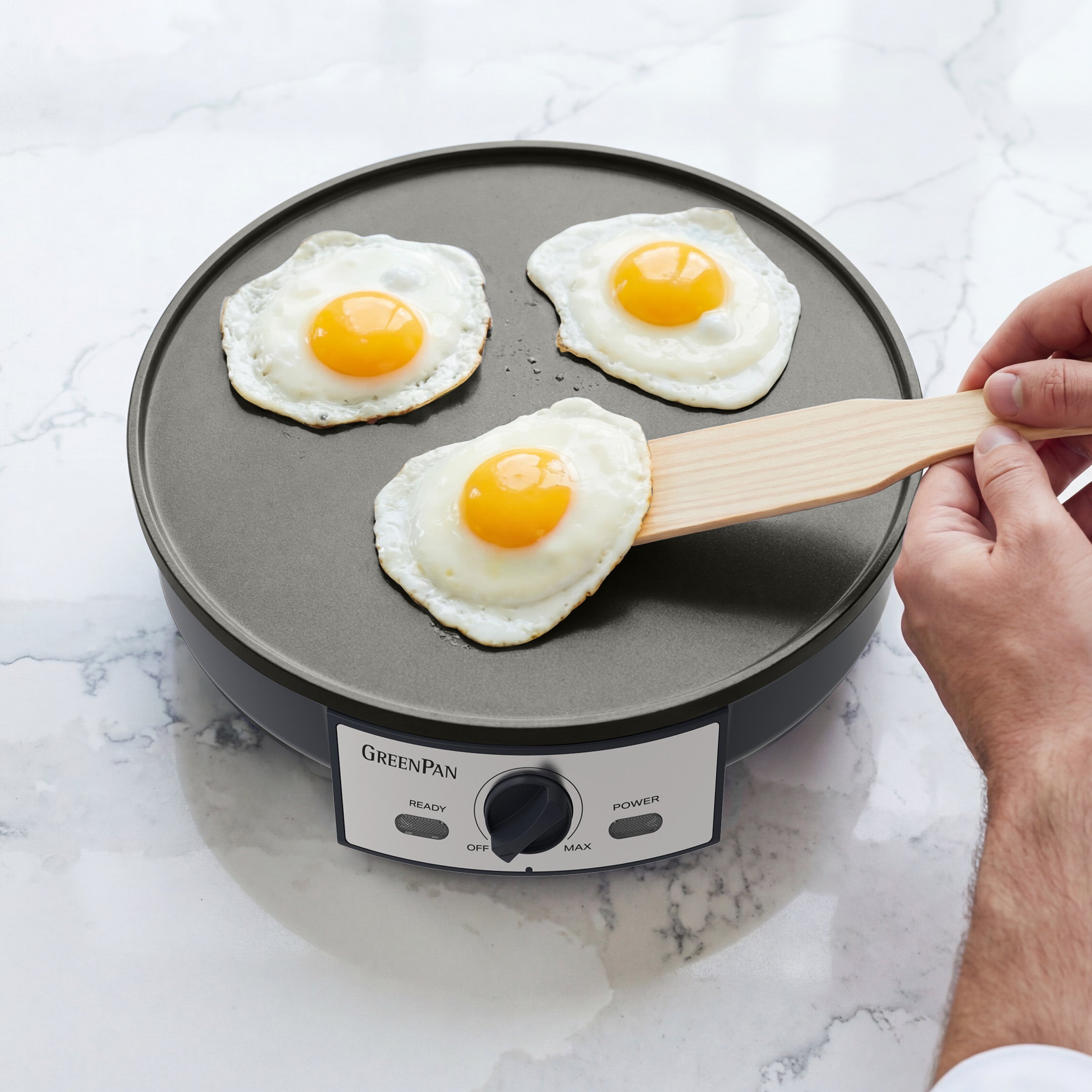 Person flipping eggs on a GreenPan electric crepe maker on a marble countertop