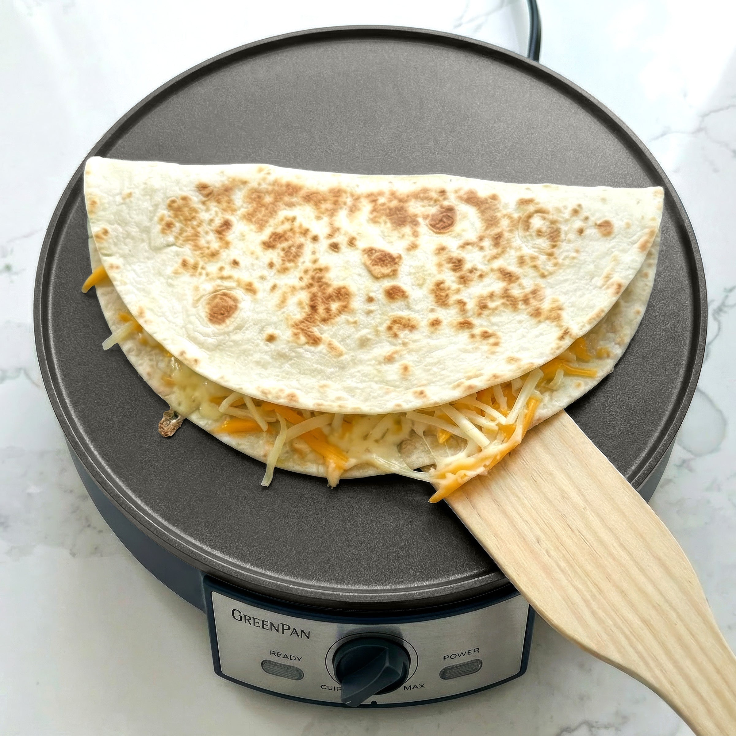 Quesadilla being made on a GreenPan electric crepe maker with cheese and tortilla