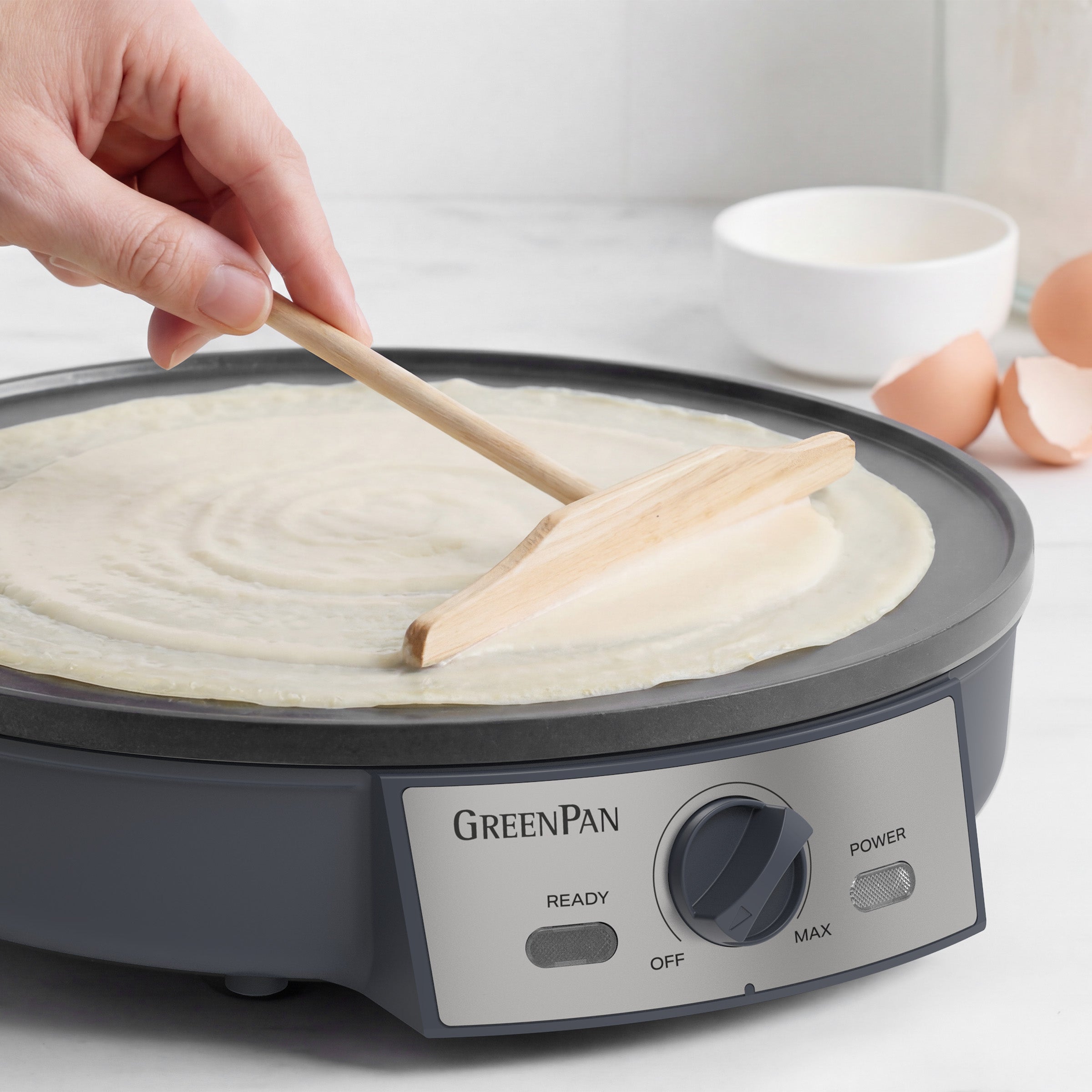 Person using a wooden spatula to spread batter on a GreenPan crepe maker.