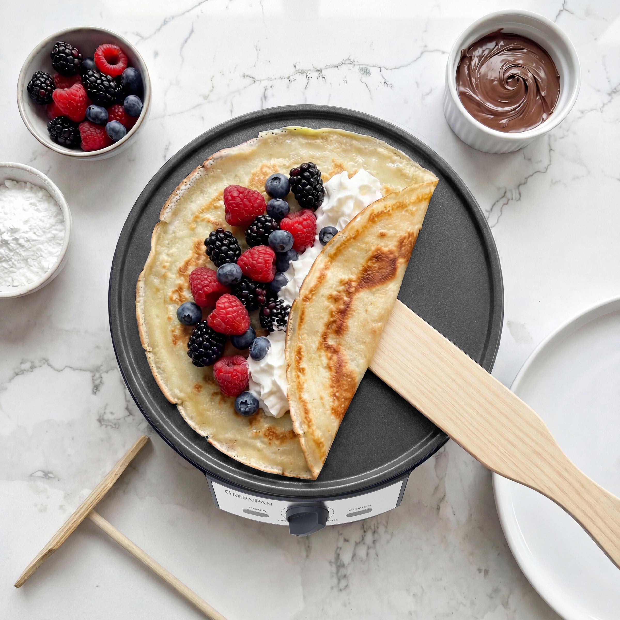 Crepe with berries on an electric crepe maker with ingredients around