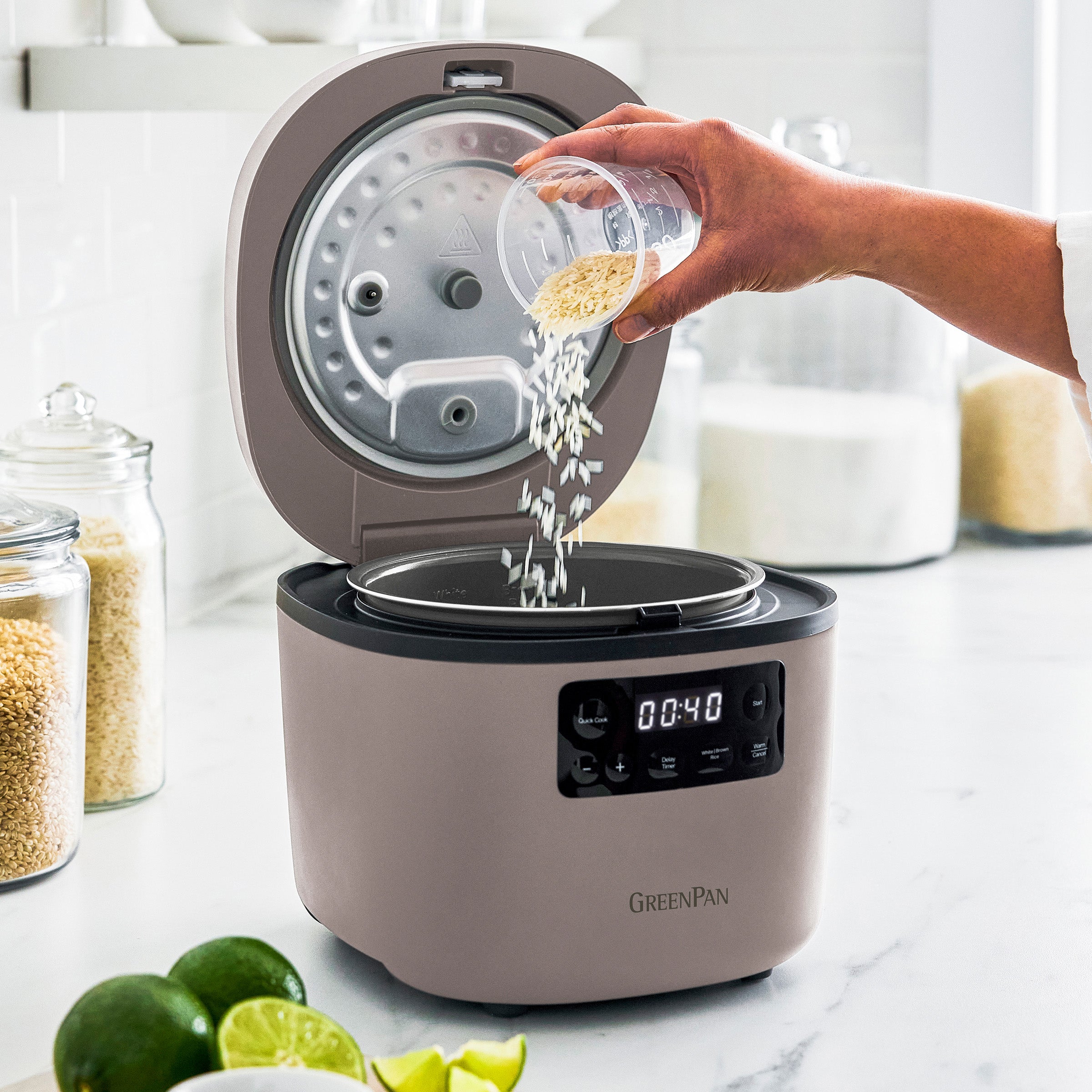 Person adding rice to a GreenPan rice cooker on a kitchen counter.