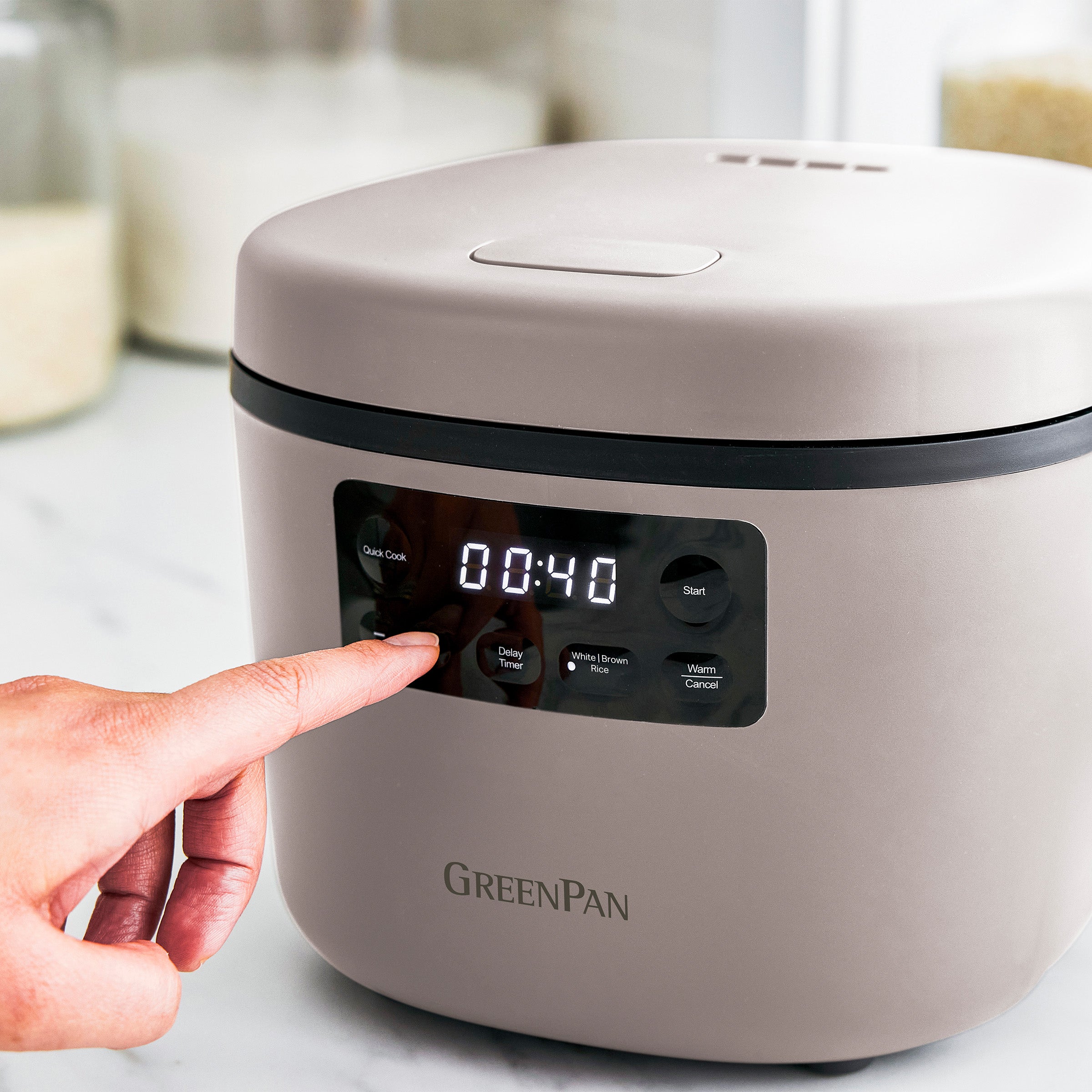 Person pressing a button on a taupe GreenPan rice cooker.