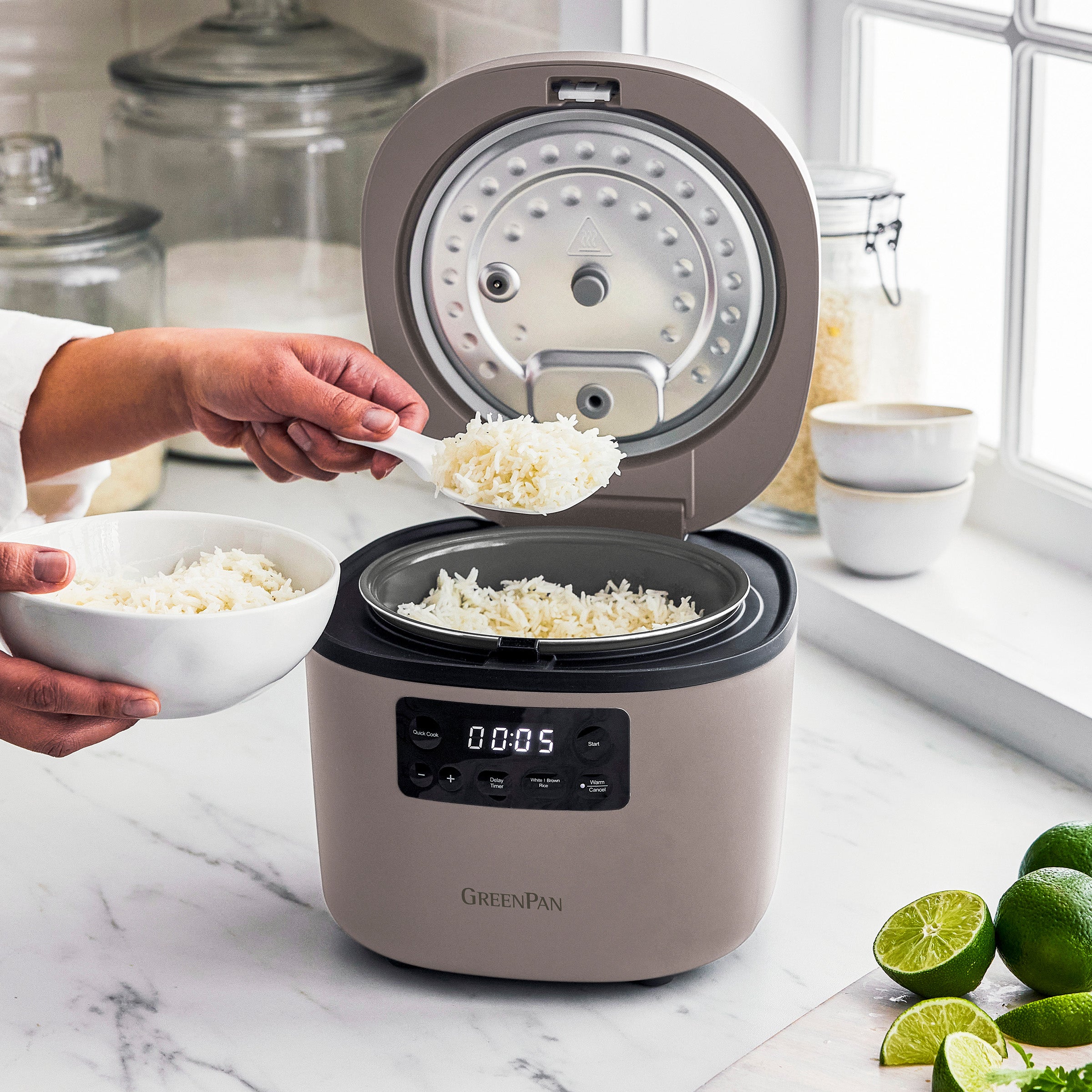 Person using a GreenPan rice cooker on a kitchen counter with limes and cilantro.