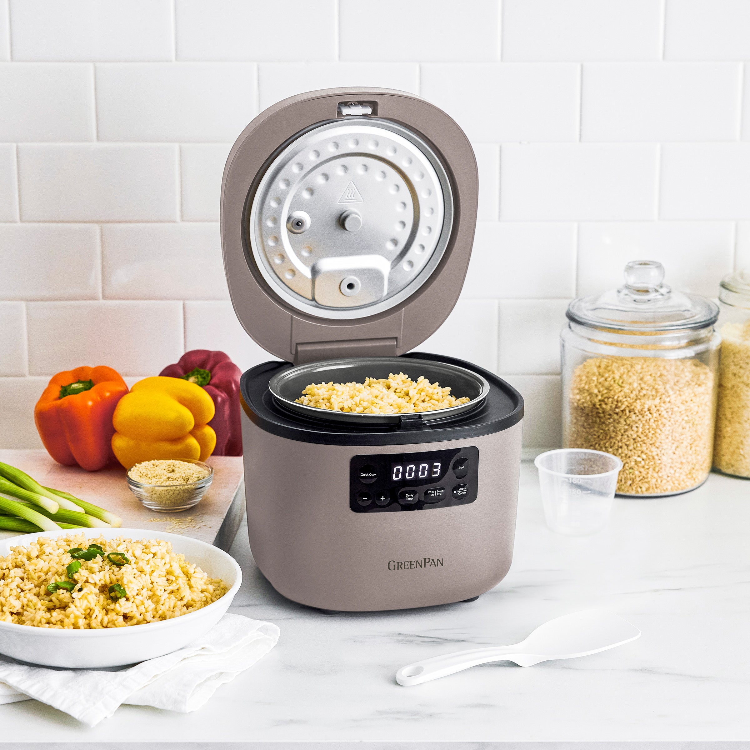 Electric rice cooker with a bowl of cooked rice on a kitchen counter.