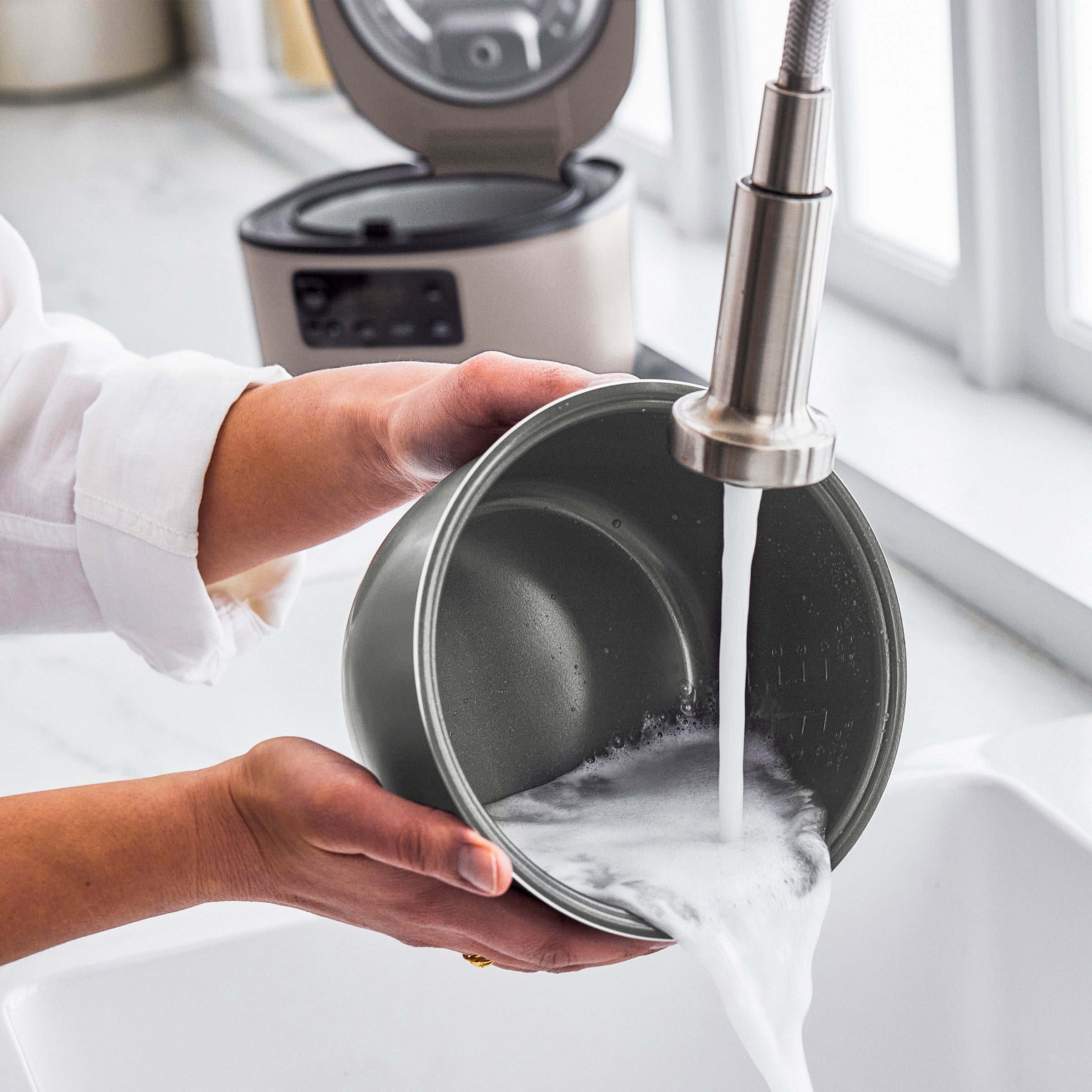 Person washing a pot under running water in a kitchen.