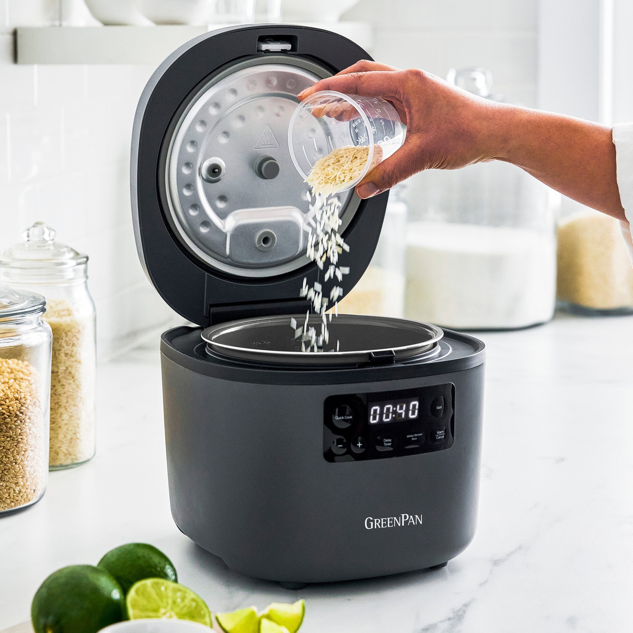 Person pouring rice into a gray GreenPan rice cooker on a kitchen counter.