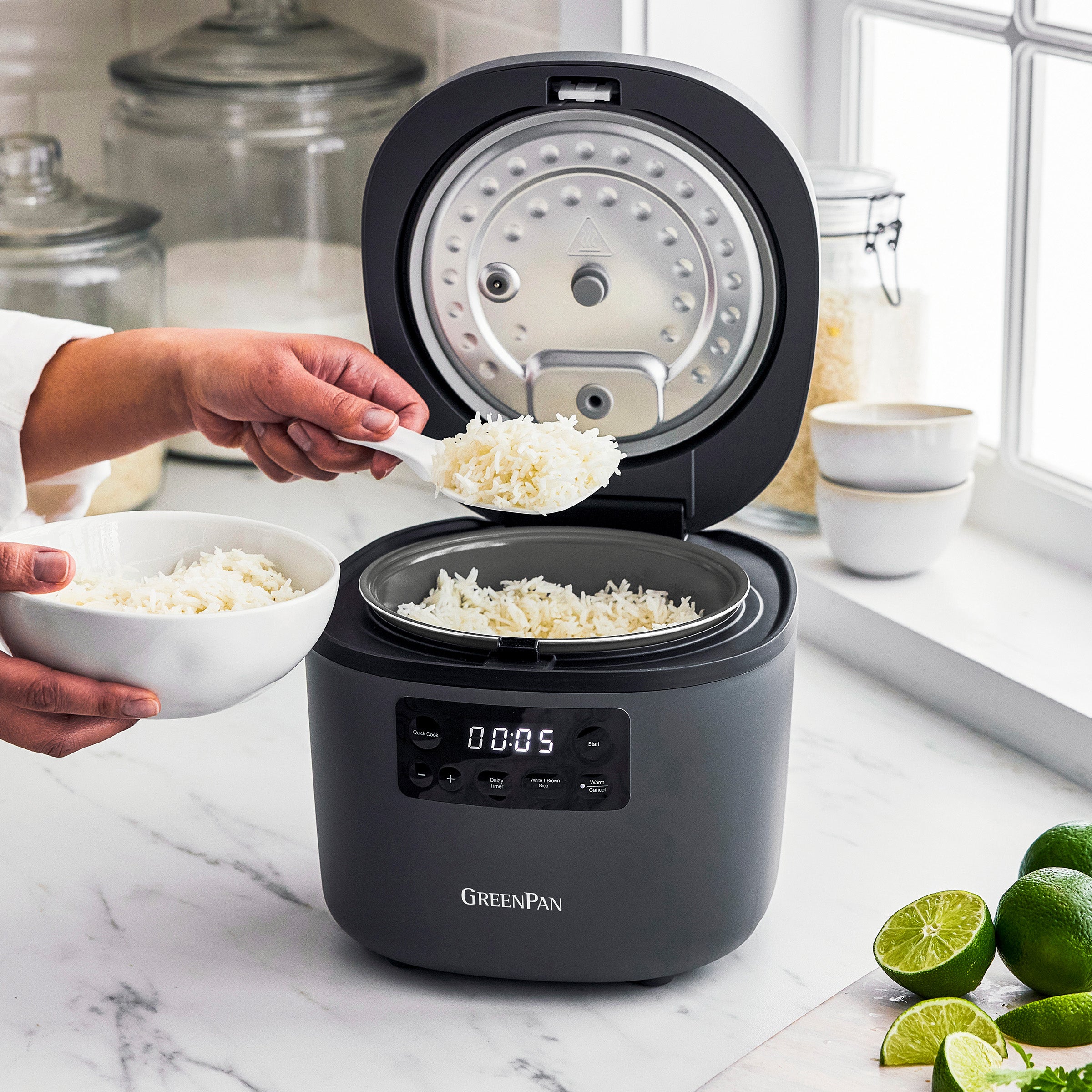 Person scooping rice from a GreenPan rice cooker on a kitchen counter.