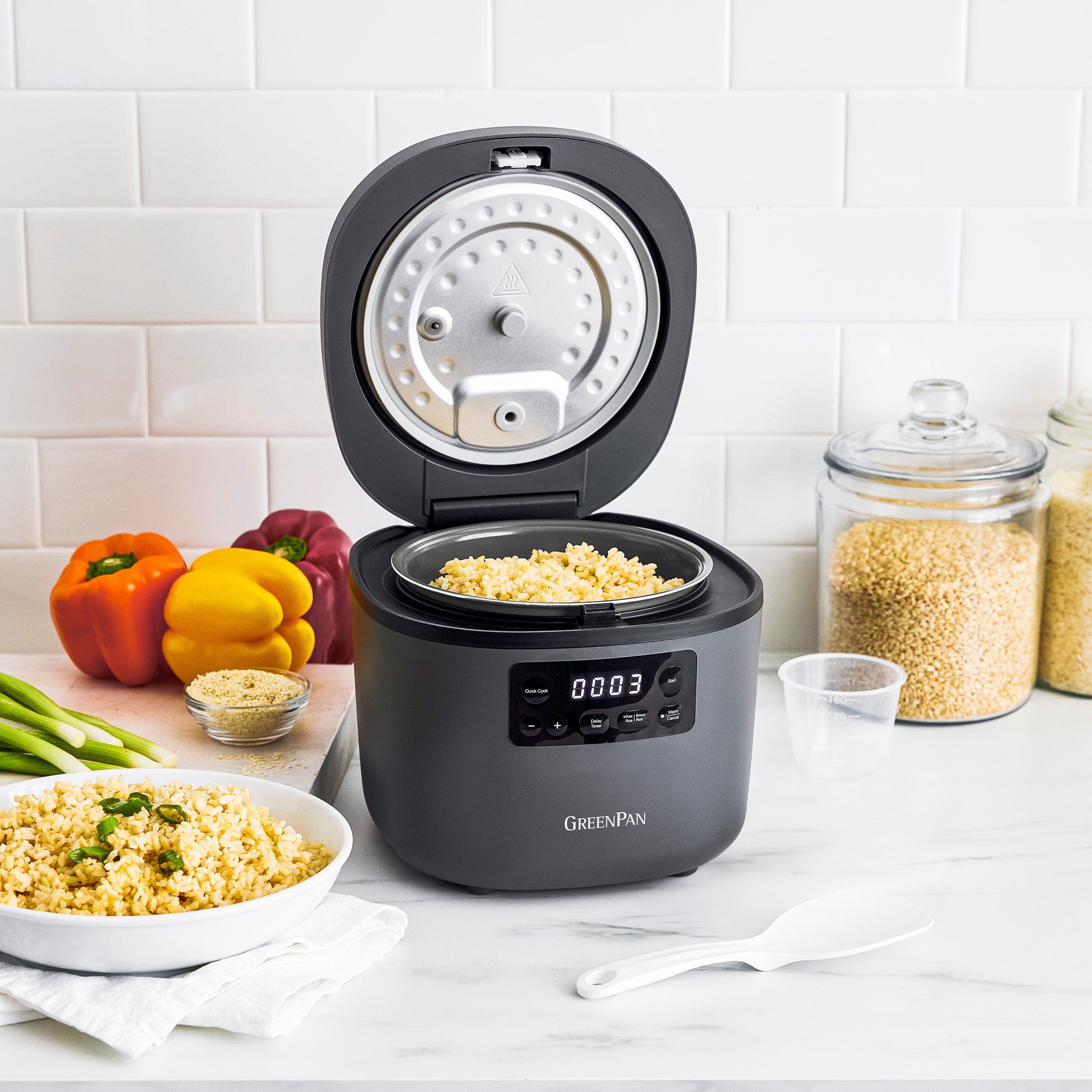 Gray rice cooker with open lid on a kitchen counter, displaying cooked rice inside.