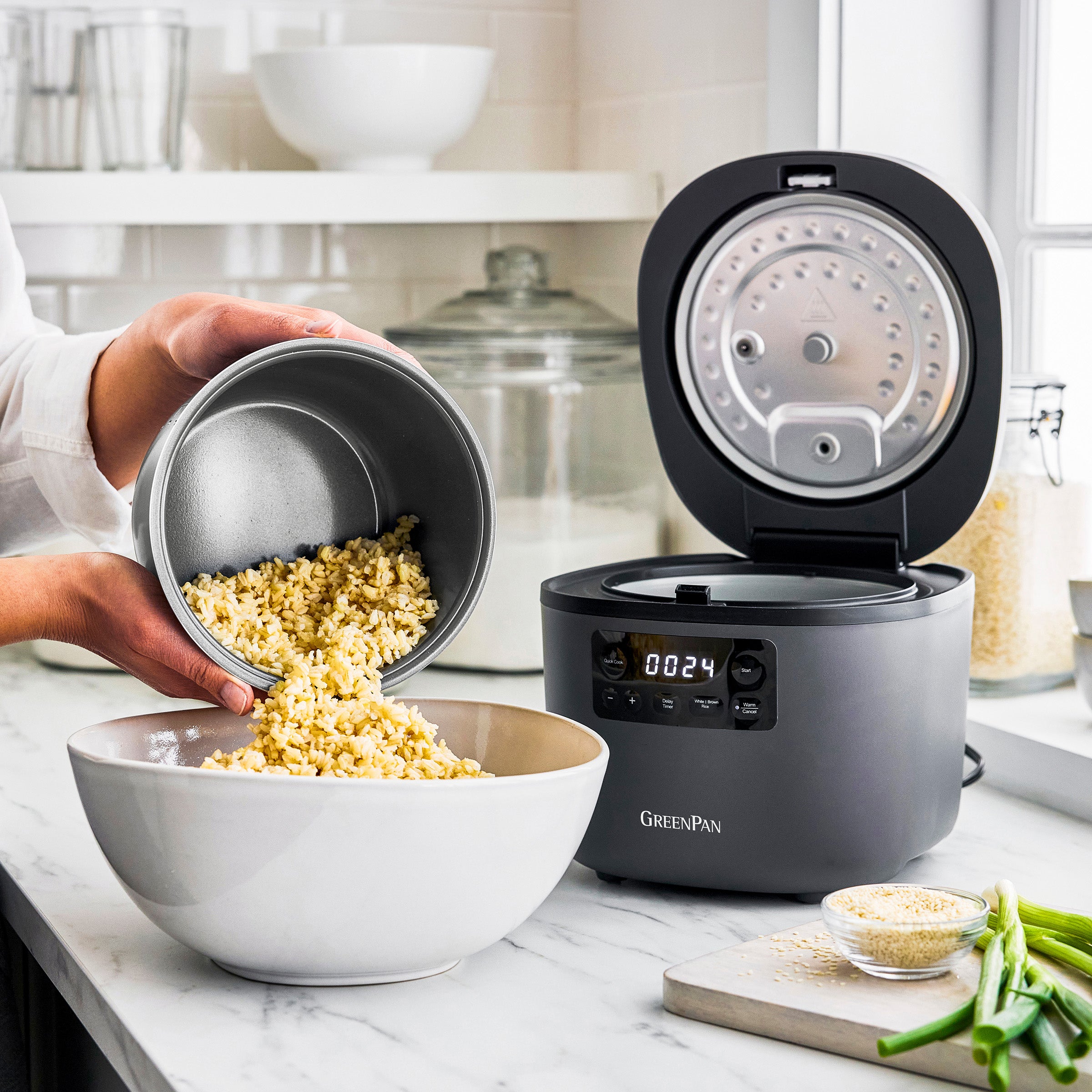 Electric rice cooker being used to make rice with a digital display on a kitchen counter.