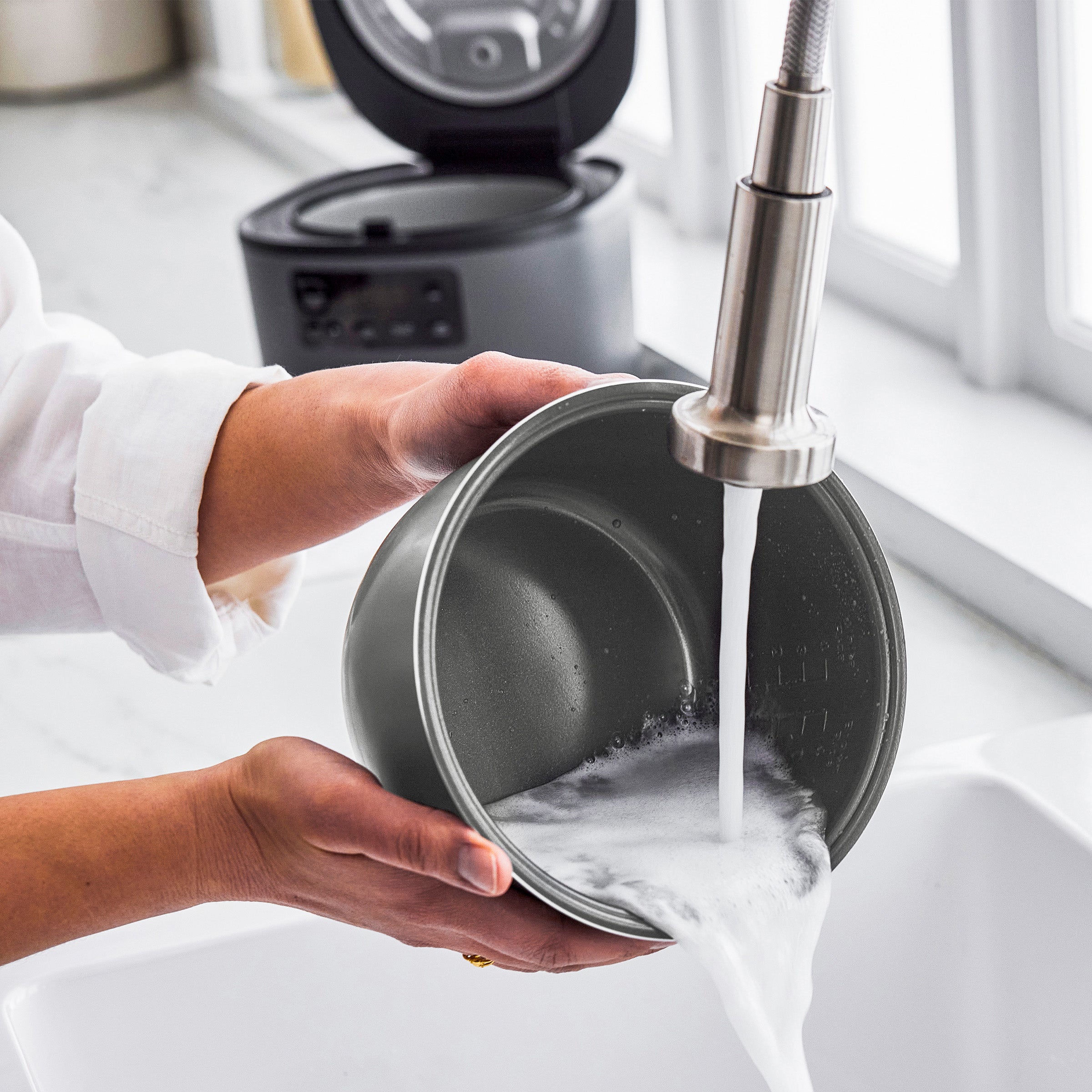 Person washing a pot under running water in a kitchen.