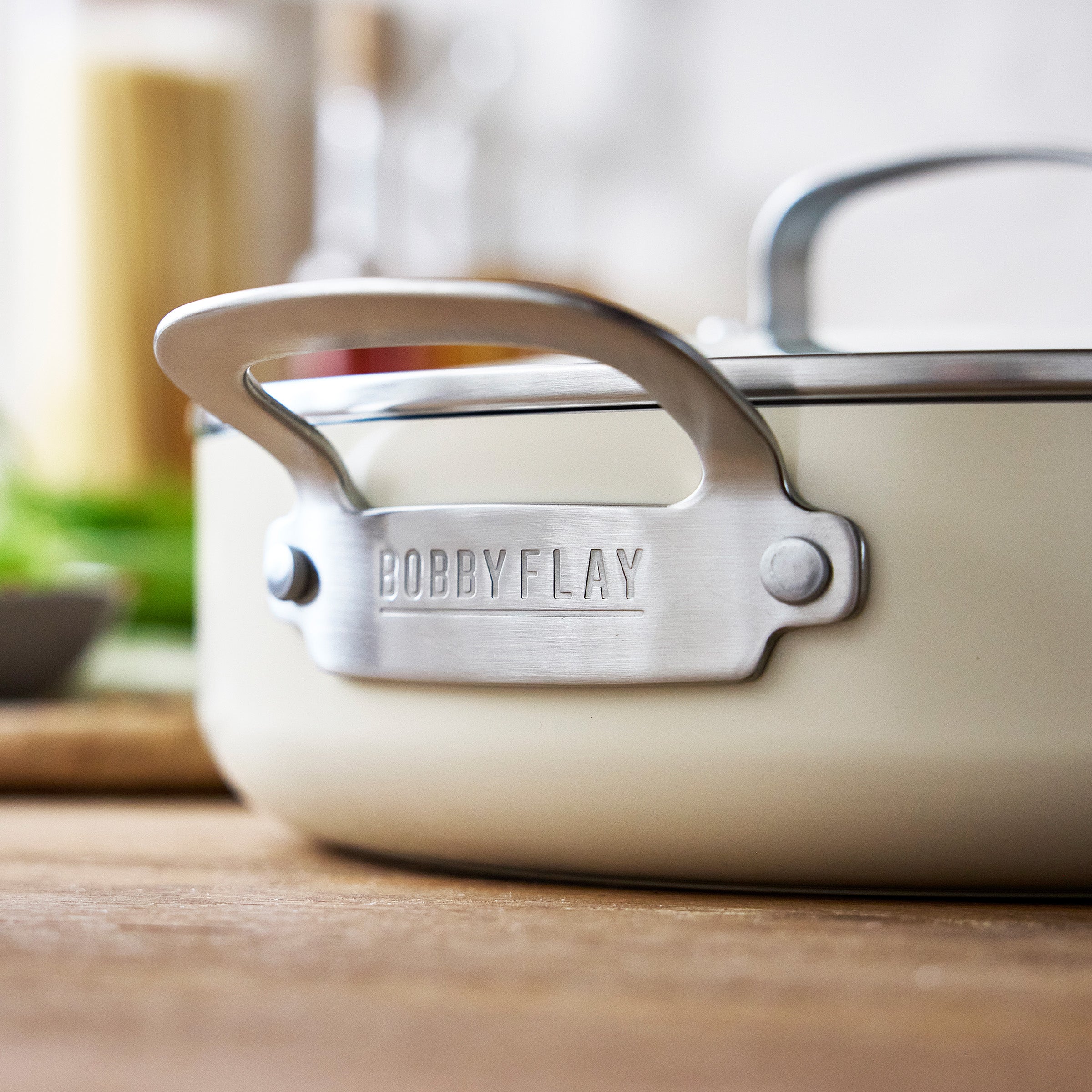 Cream-colored GreenPan pot with metal handle, made of aluminum, resting on a wooden surface.