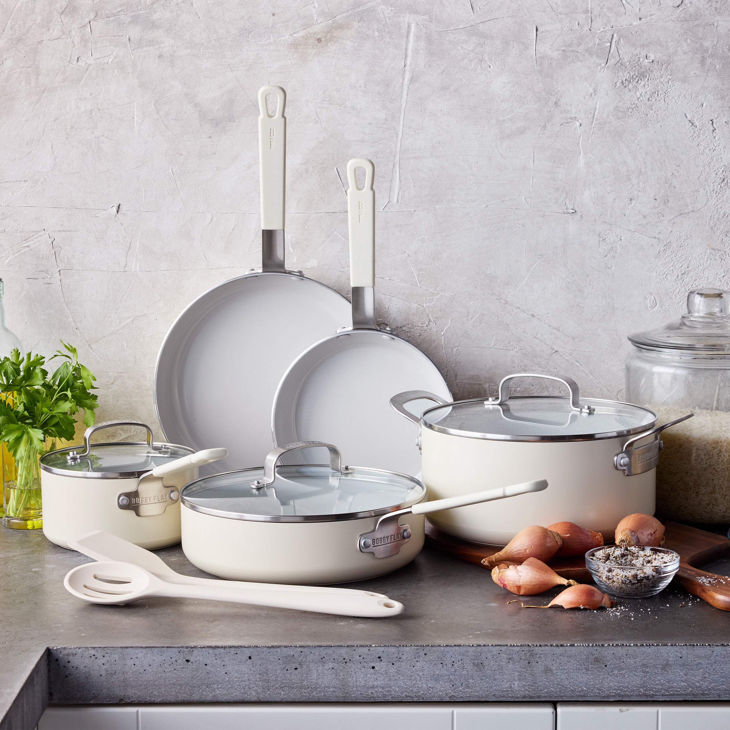 Cream ceramic 10-piece cookware set on a counter with shallots and parsley.