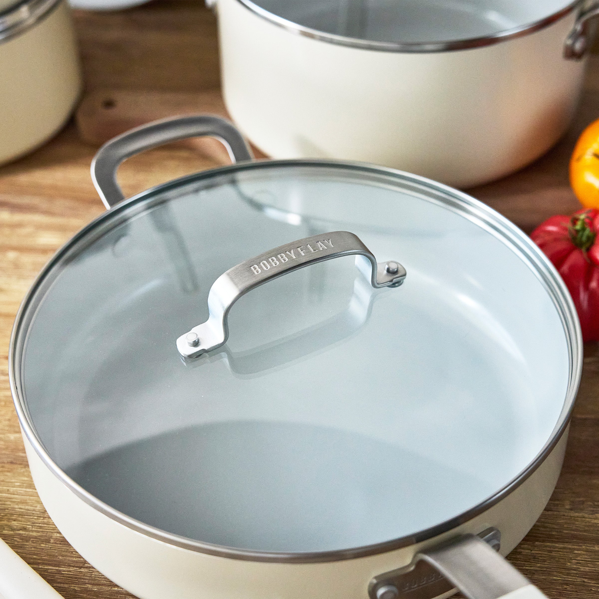 Cream ceramic nonstick 10-piece cookware set with glass lids and aluminum handles, all pieces displayed.