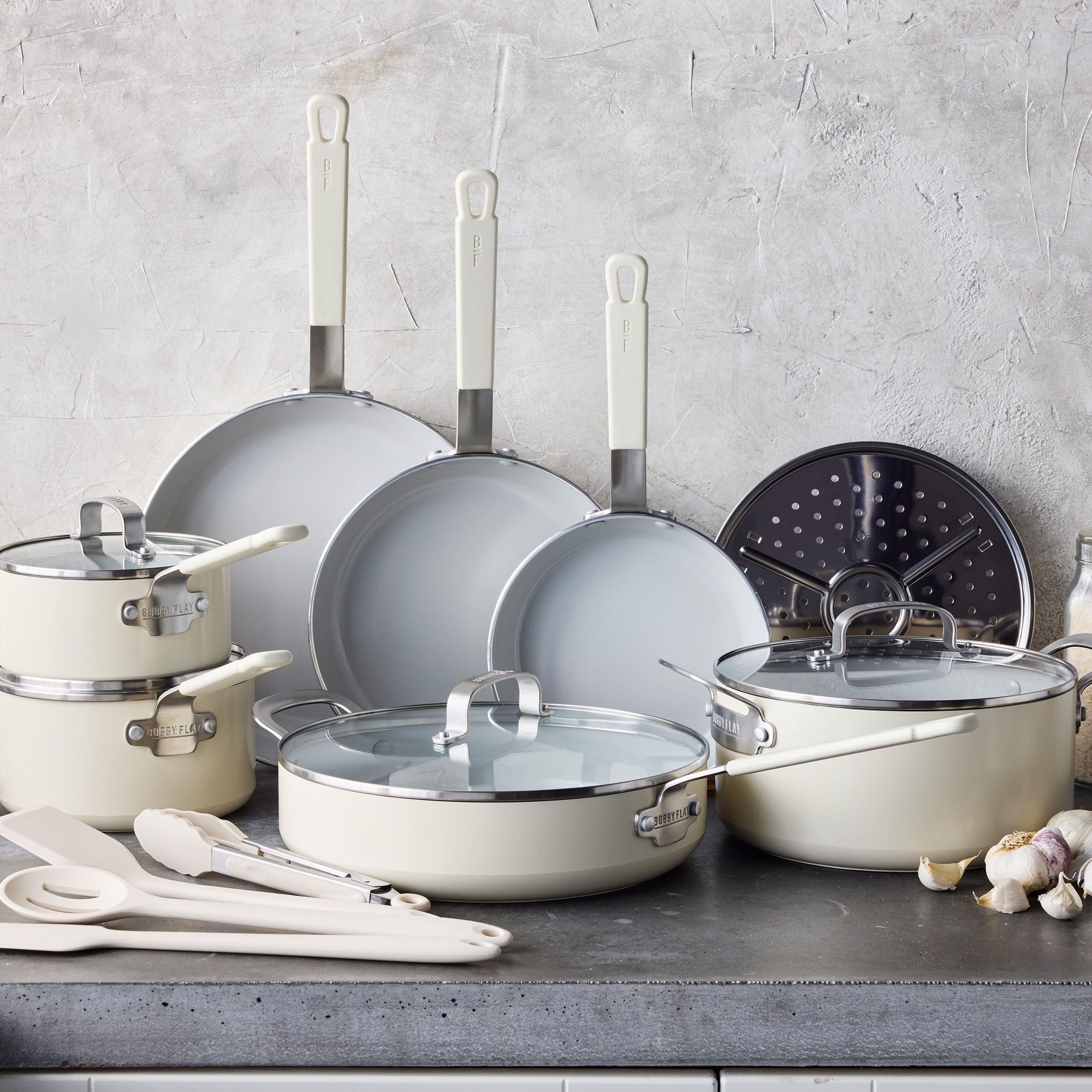 Cream 16-piece cookware set with lids and utensils on a gray countertop; features aluminum construction.