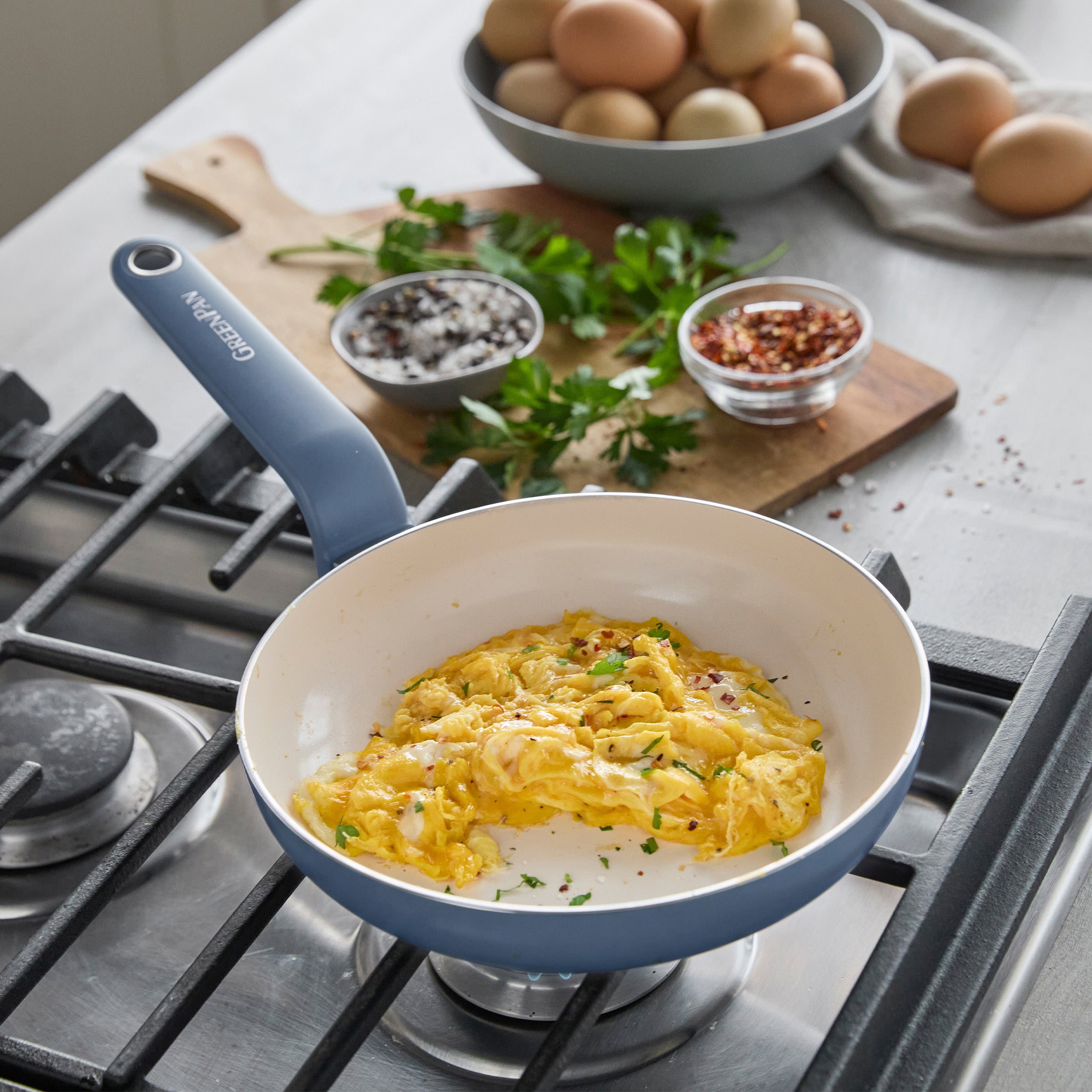 Ceramic nonstick 8-inch frypan in Dutch Blue with scrambled eggs and herbs, shown on a wooden cutting board.