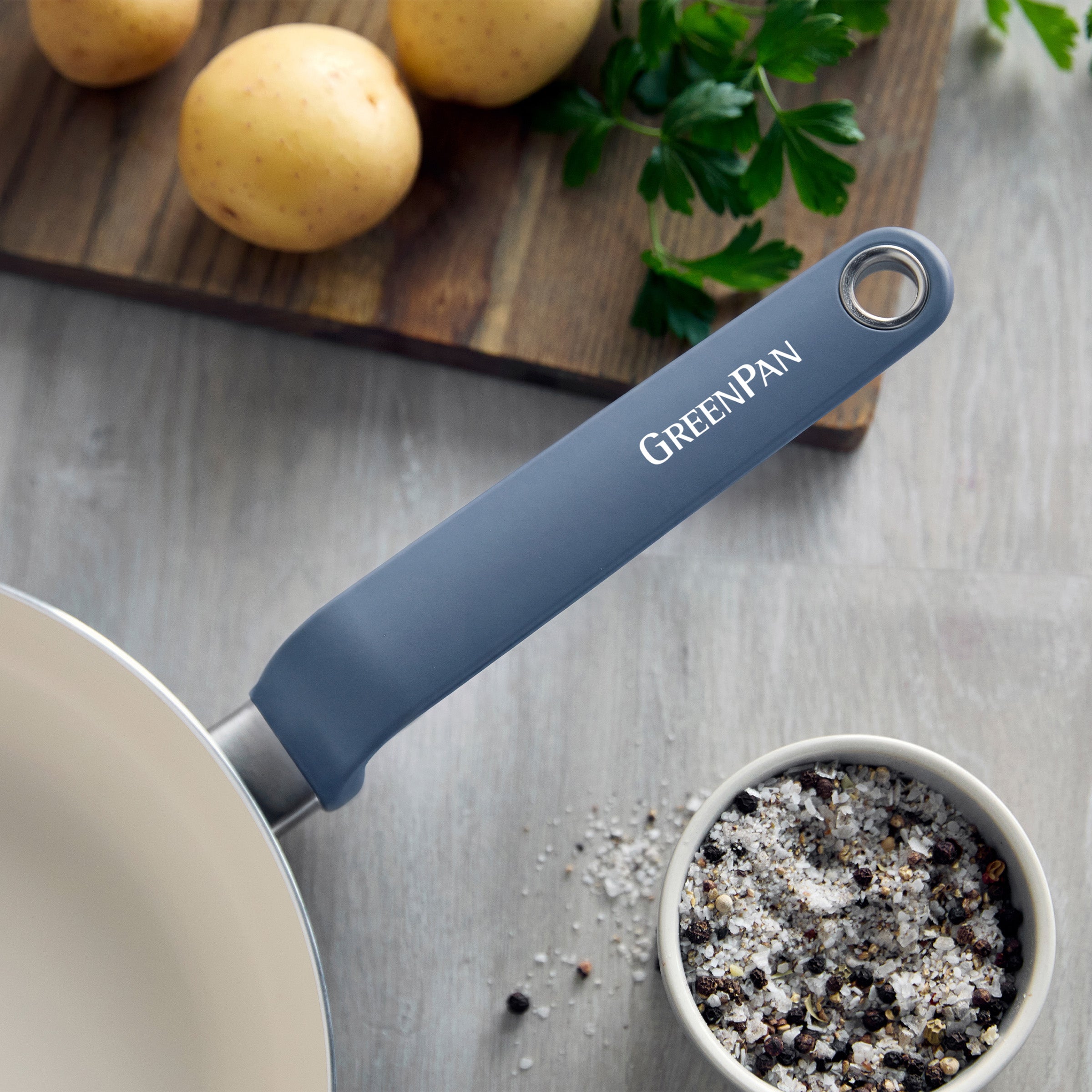 Blue ceramic 10-inch frypan on a light counter with potatoes, parsley, and salt and pepper nearby.