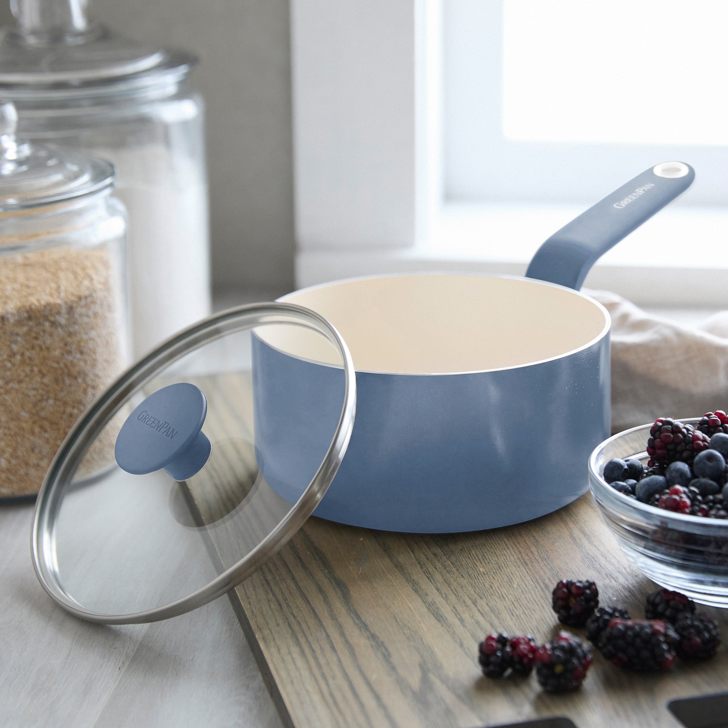Blue ceramic 2-quart saucepan with lid on a countertop next to fresh berries and oats.