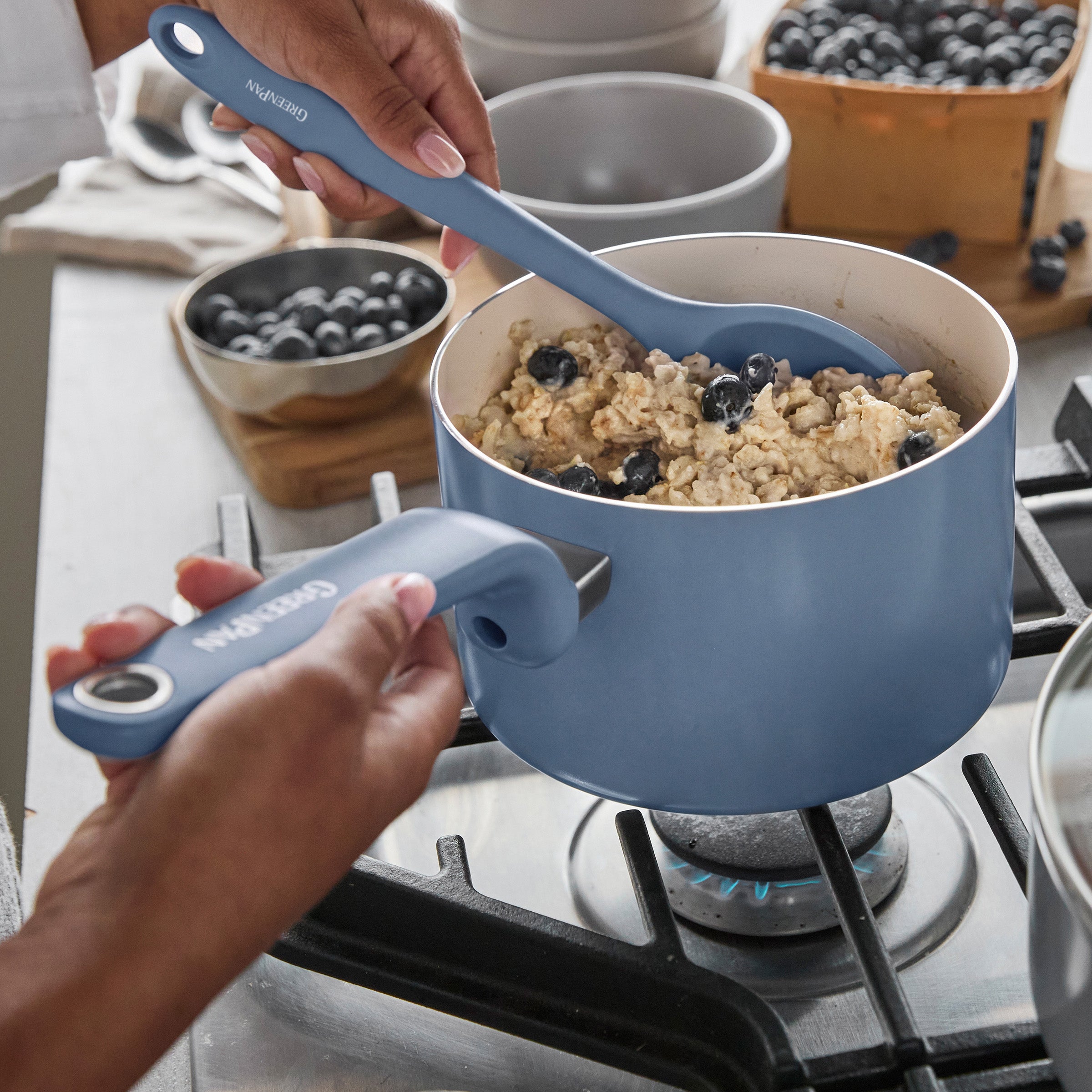Oatmeal with blueberries being stirred in a Dutch blue ceramic nonstick 2-quart saucepan on a stove.