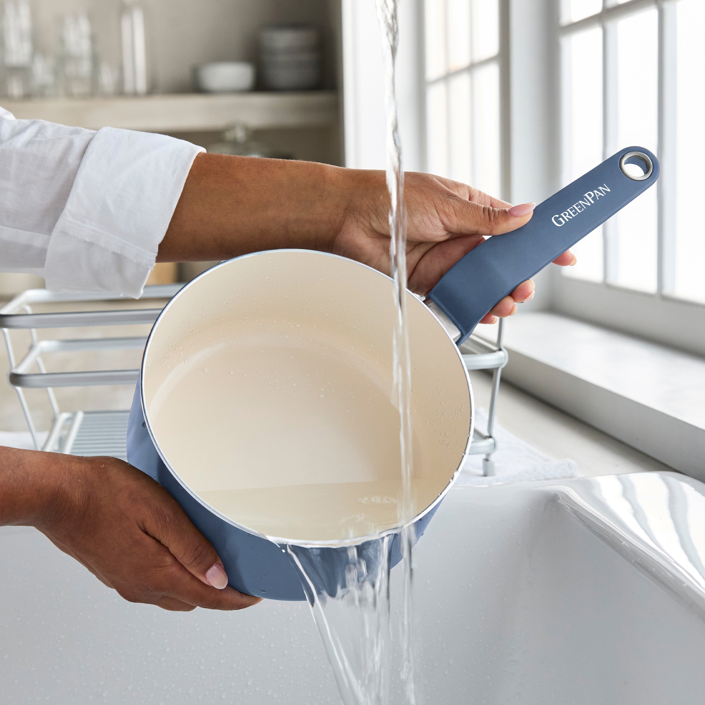 Blue ceramic nonstick 2-quart saucepan being filled with water at a kitchen sink.