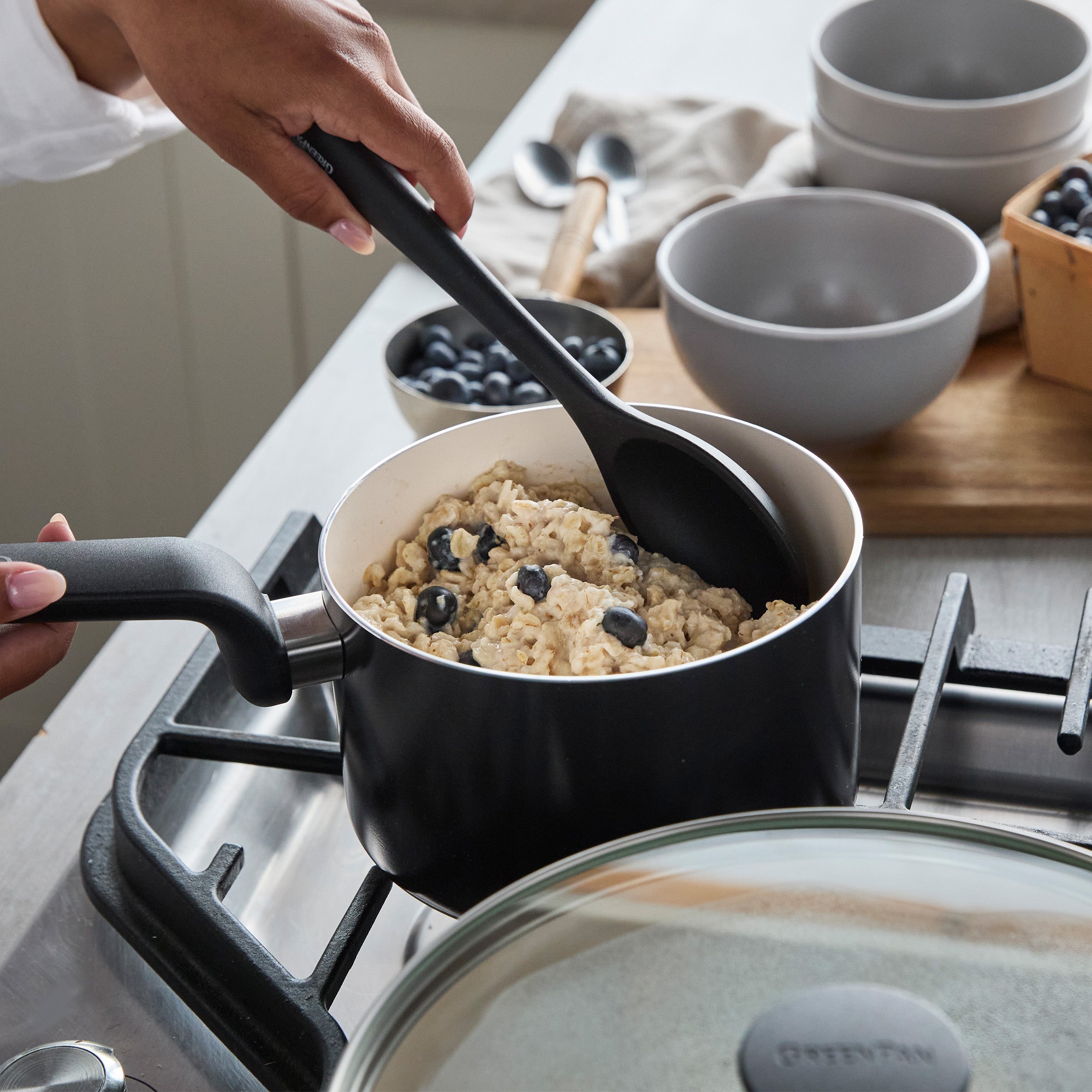 Blueberry oatmeal being stirred in a black nonstick pot from the Rio Advanced Ceramic 12-piece cookware set on a stove.