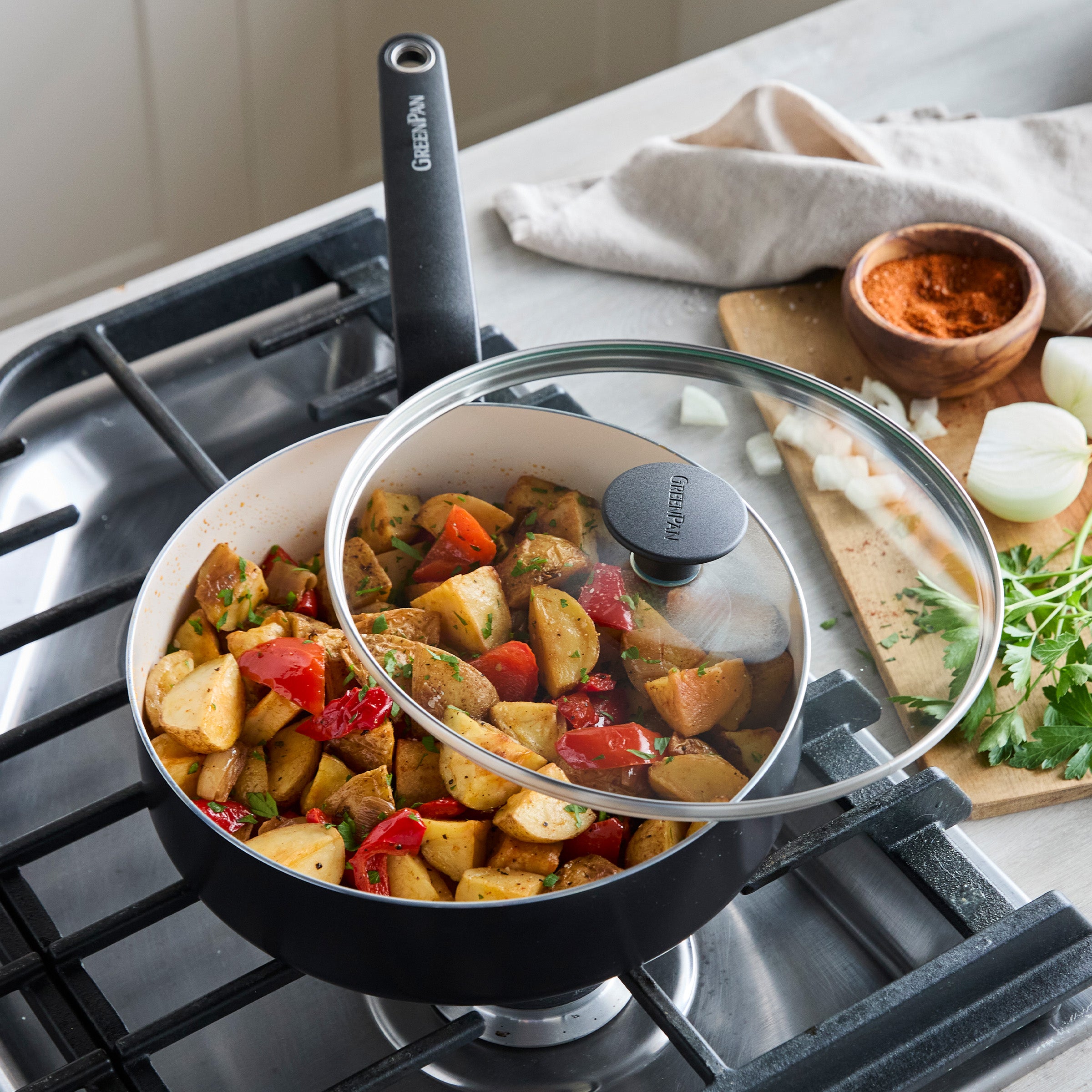 Cooked potatoes and peppers in Rio ceramic nonstick pan on stove, with herbs and spices beside cookware.