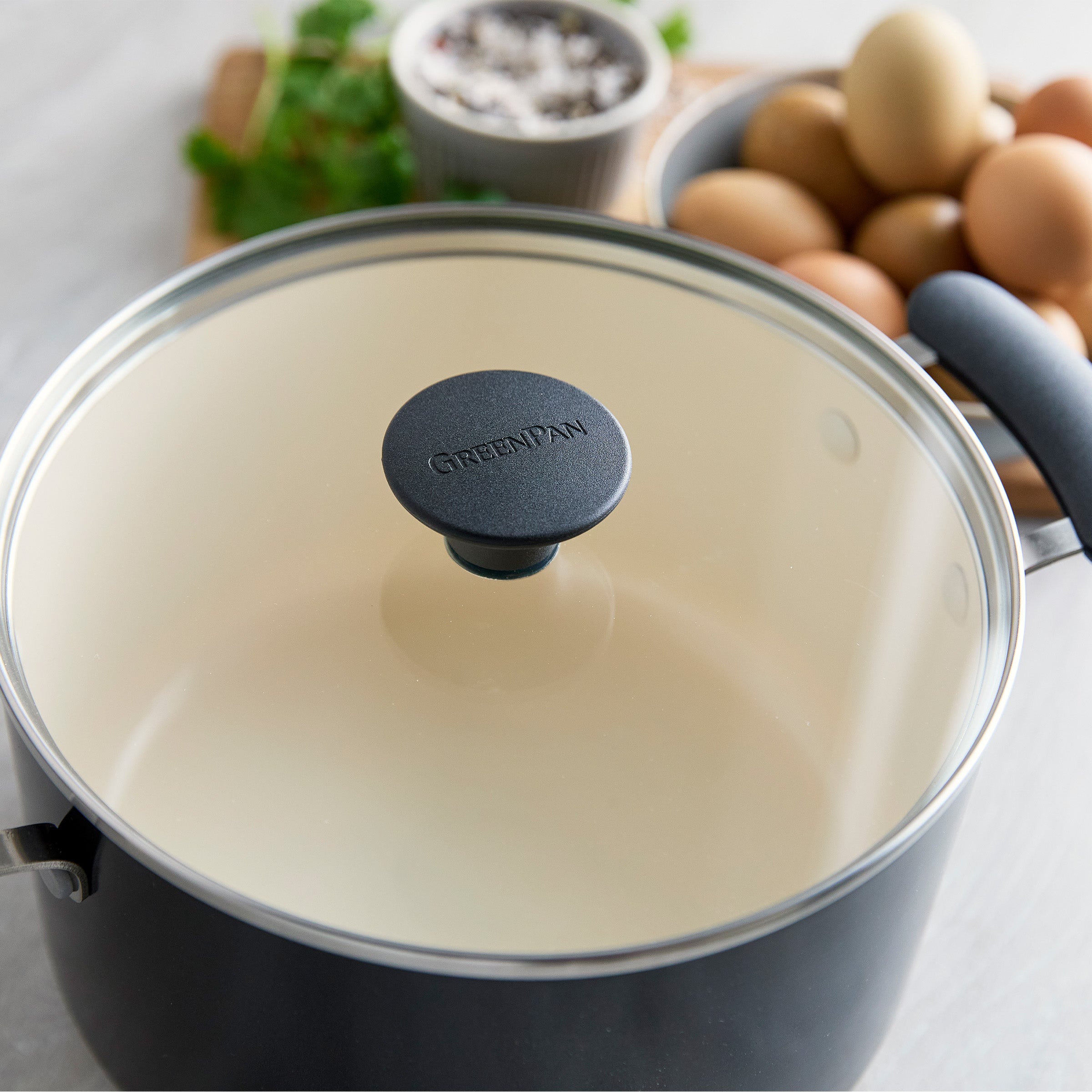 Covered Rio ceramic nonstick pot from a 12-piece set on a counter with eggs and a small dish of seasoning.