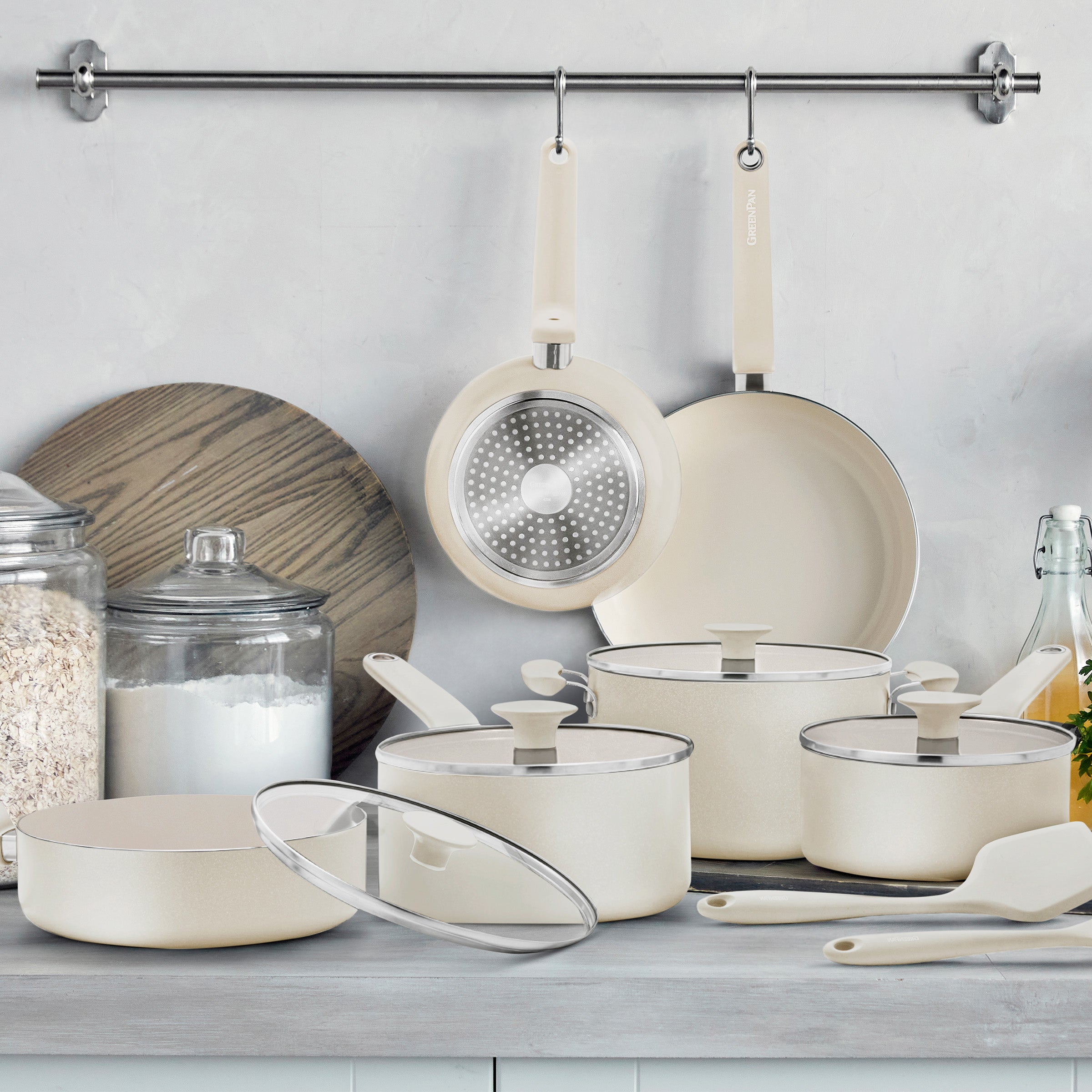 Cream ceramic nonstick 12-piece cookware set with pans, utensils, glass jars, and a wooden tray arranged together.