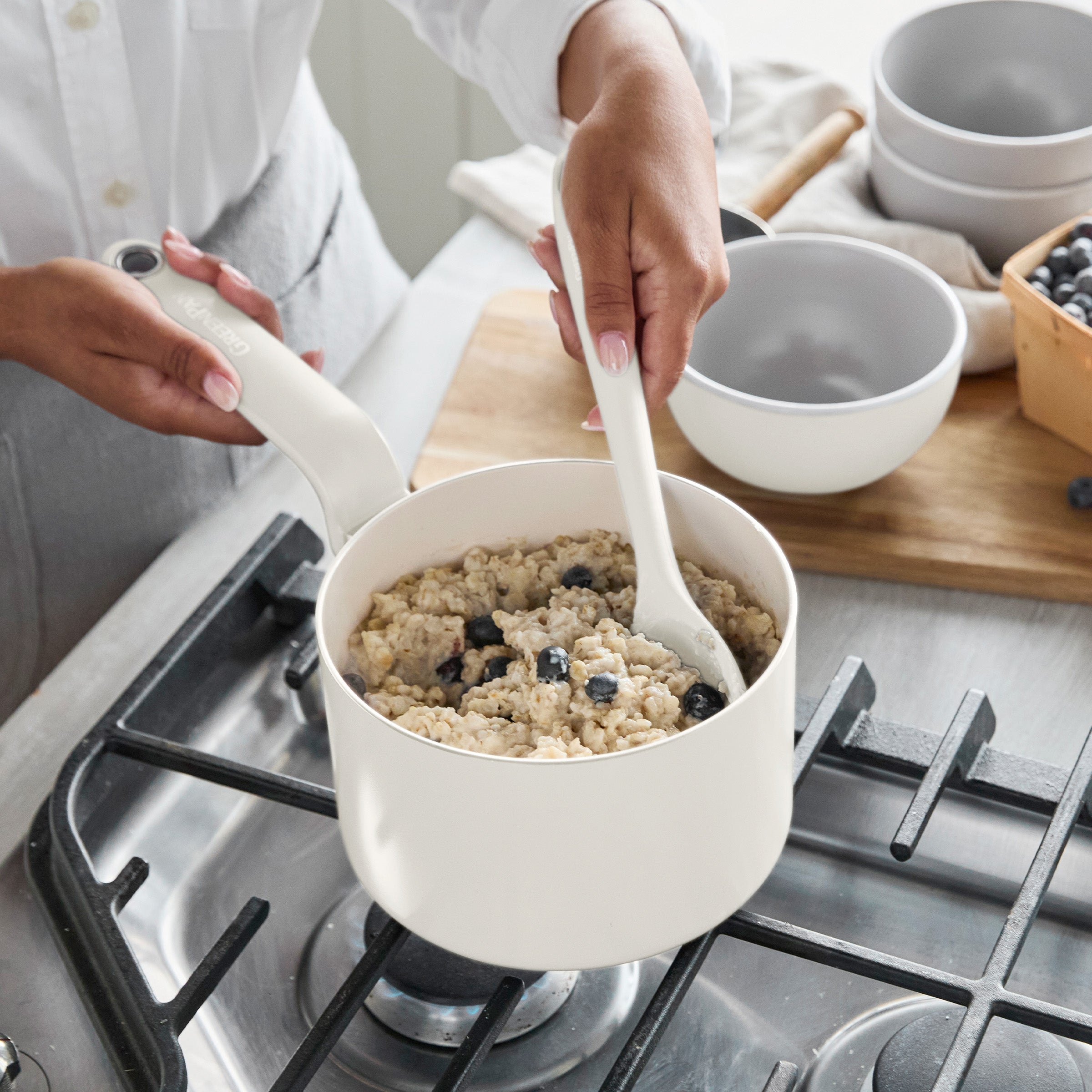 Blueberry oatmeal being stirred in a cream-colored nonstick saucepan from the 12-piece Rio Advanced Ceramic Cookware Set on a stove.