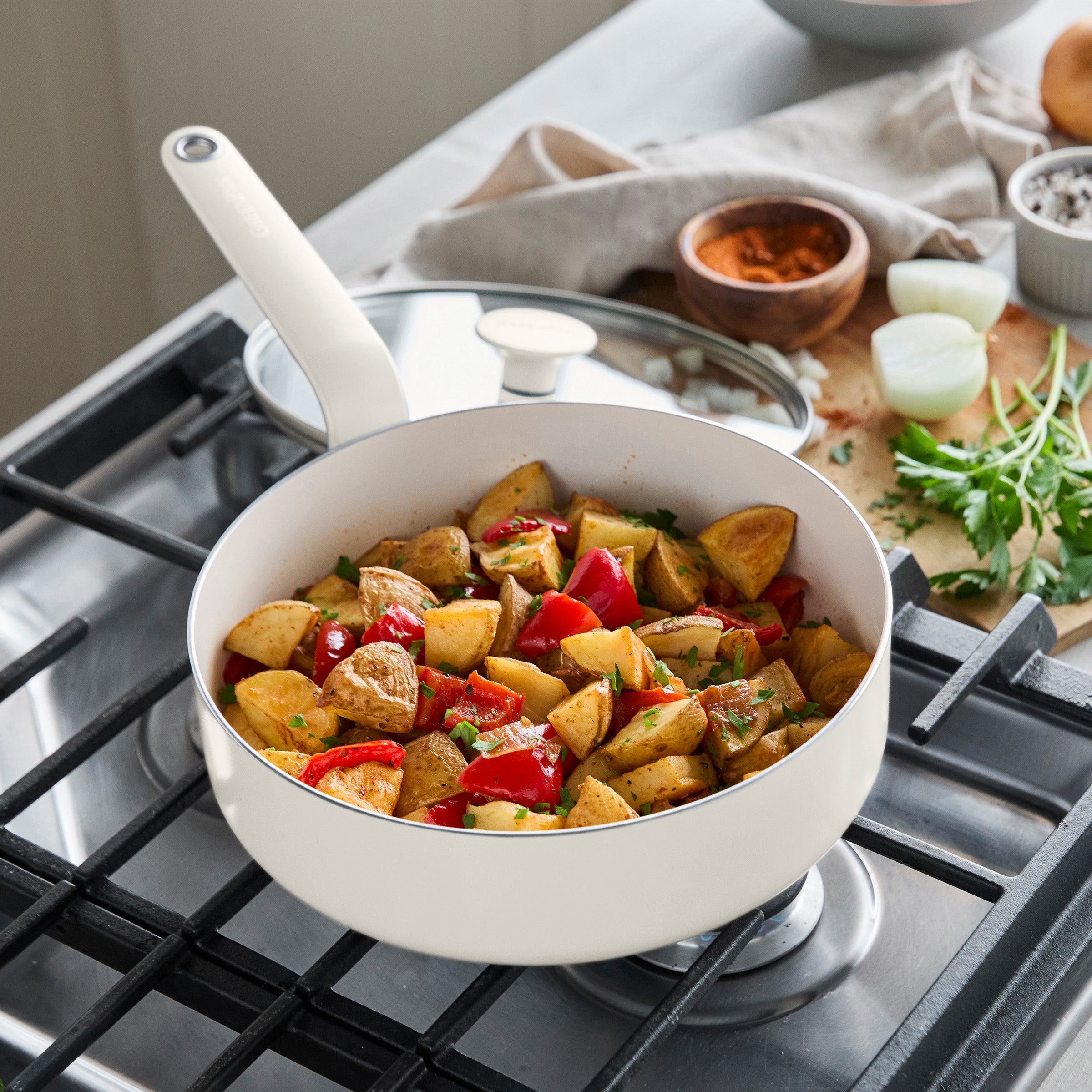 Cream ceramic nonstick cookware on a stove, filled with roasted potatoes, red peppers, and herbs.
