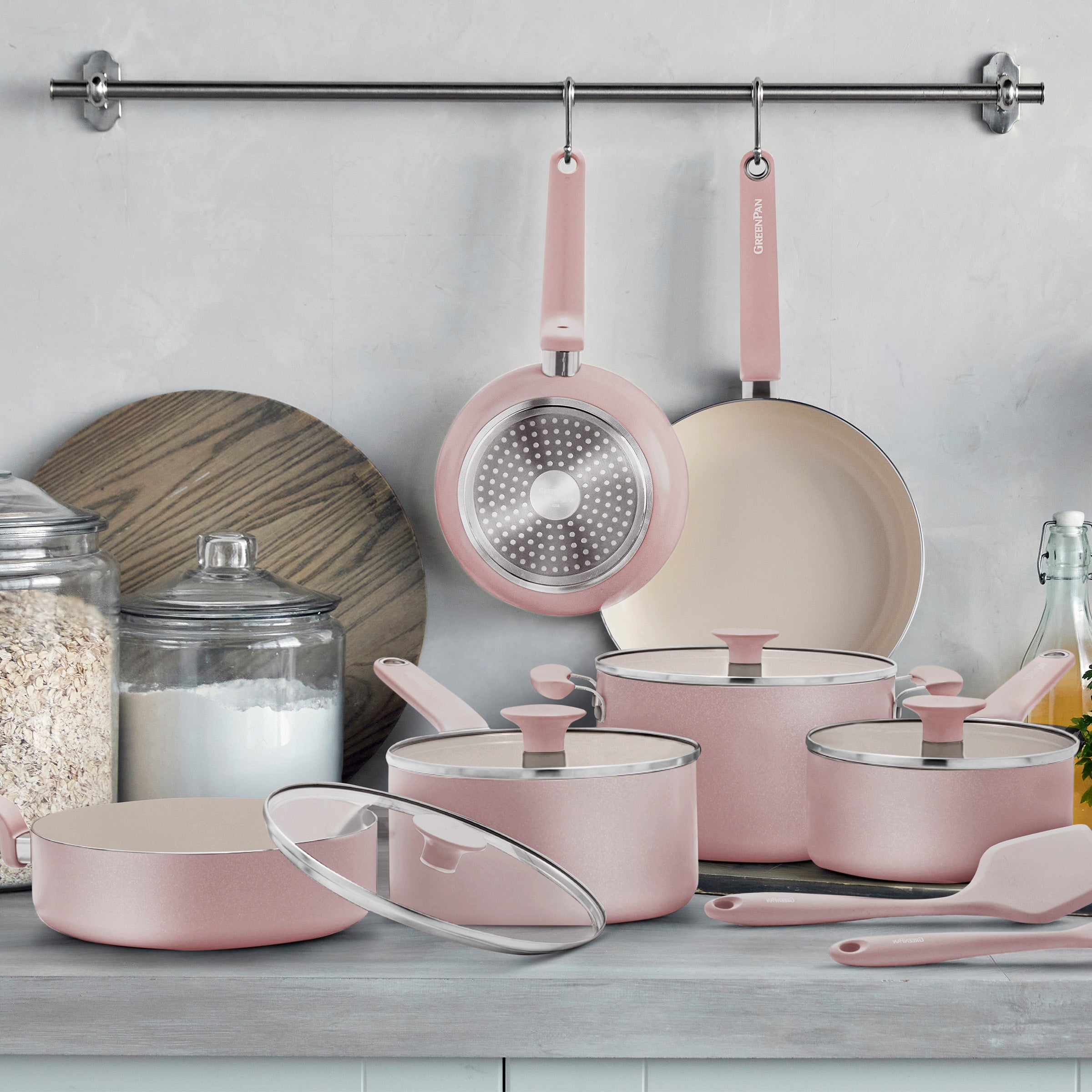 Pink ceramic cookware set with pots, pans, and glass lids arranged on a kitchen counter, 12 pieces total.