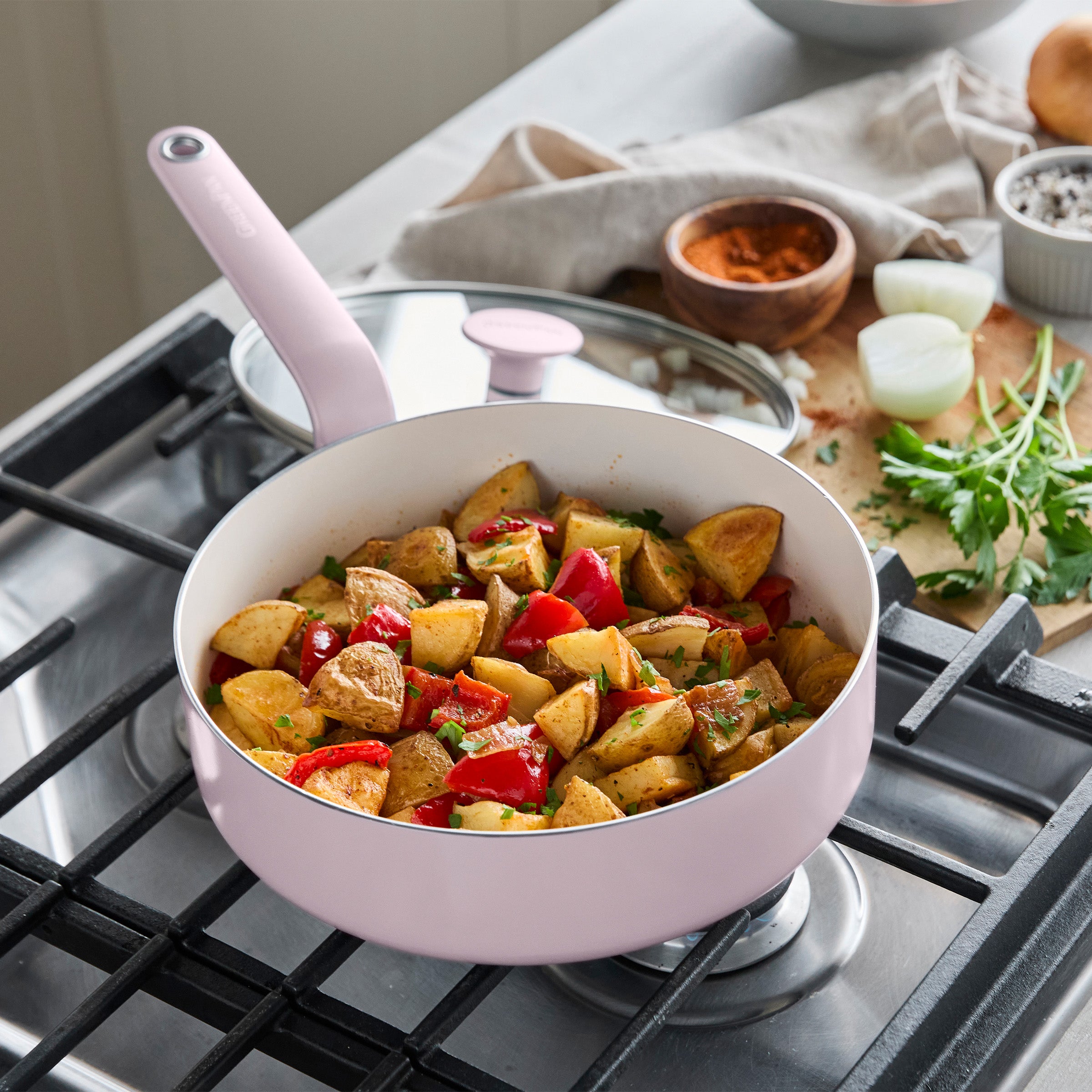 Pink ceramic 12-piece cookware set with roasted potatoes and red peppers, topped with fresh herbs.